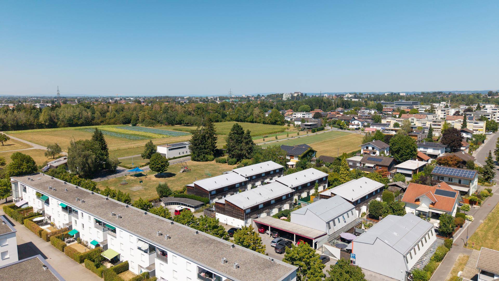 Luftaufnahme einer Wohnsiedlung mit angrenzenden Feldern und weitem Blick in die Landschaft.
