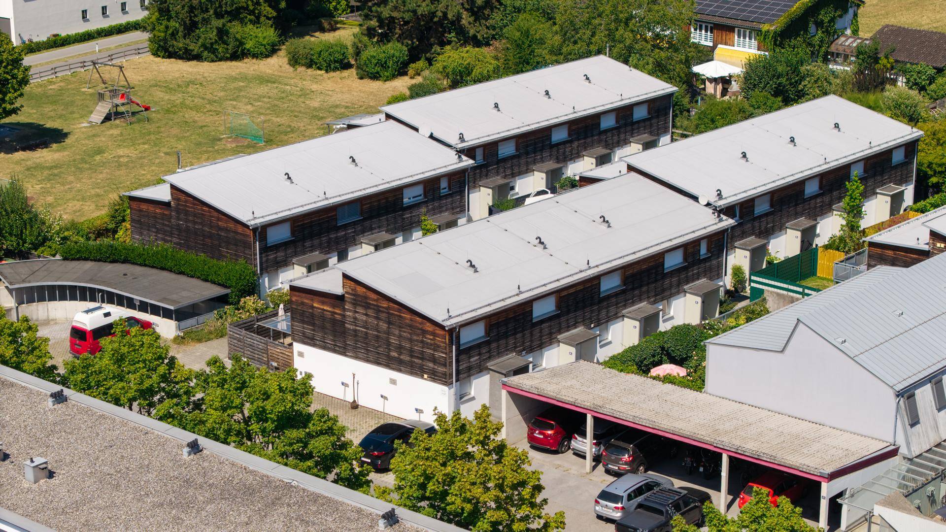 Luftaufnahme einer Wohnsiedlung mit Reihenhäusern, Flachdächern und überdachten Parkplätzen.