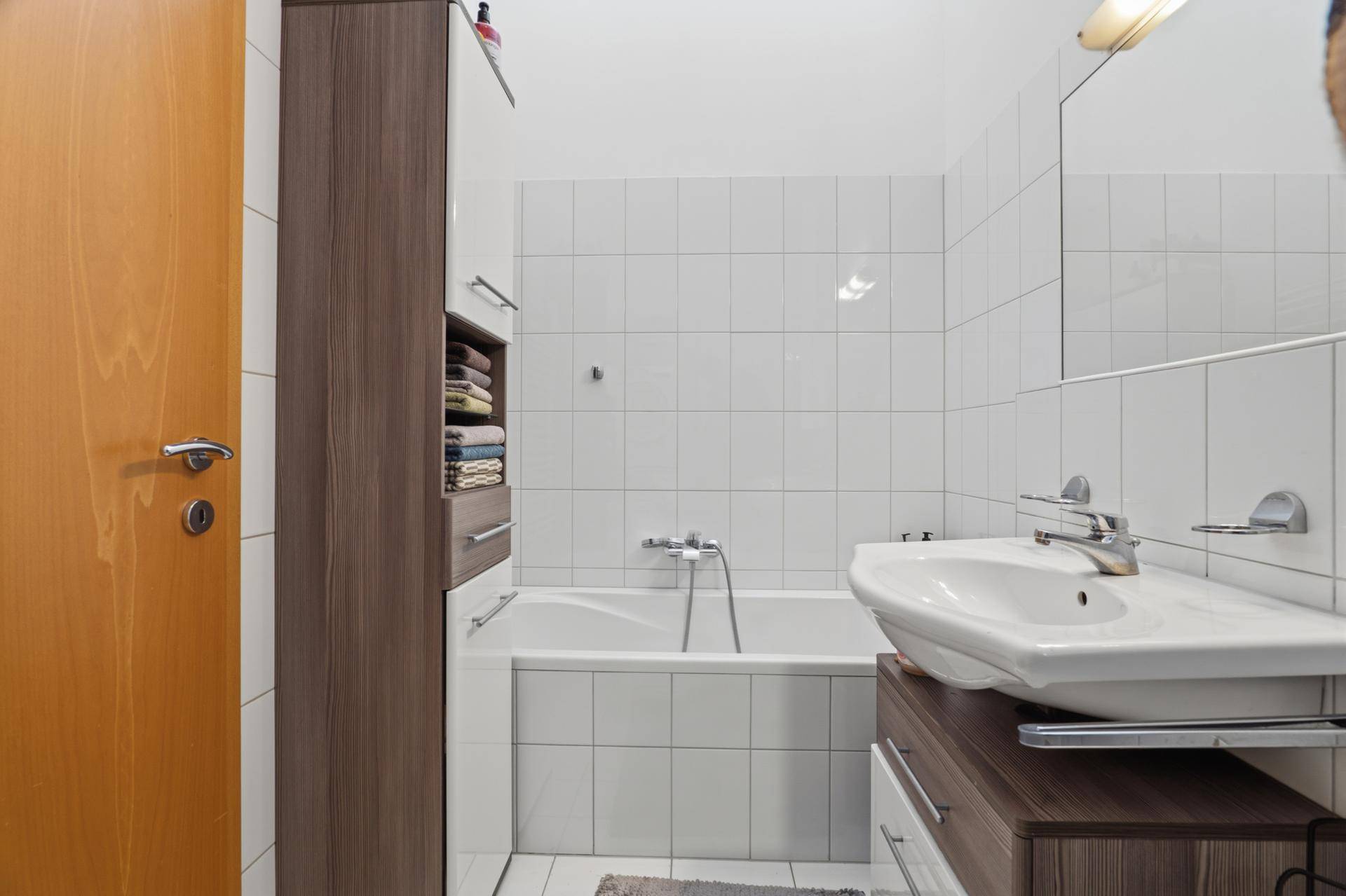 Helles Badezimmer mit Badewanne, modernem Waschbecken und praktischem Hochschrank.