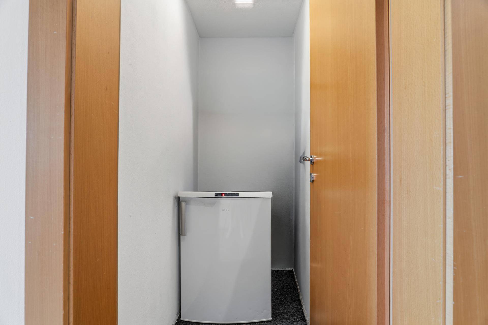 Kleiner Abstellraum mit Gefrierschrank und Holztüren.