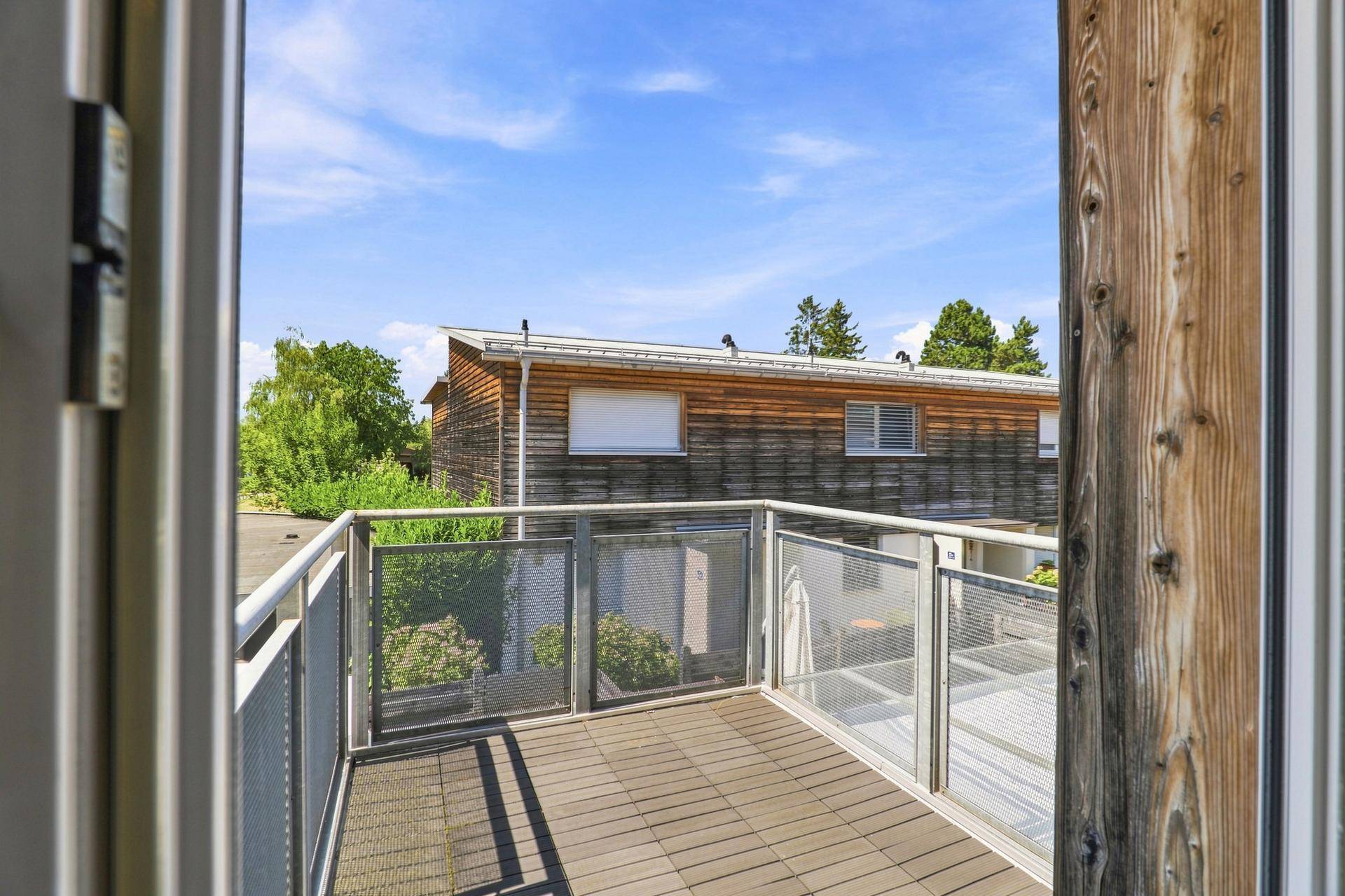Geräumiger Balkon mit Holzboden und Metallgeländer, bietet einen Blick auf die Umgebung.