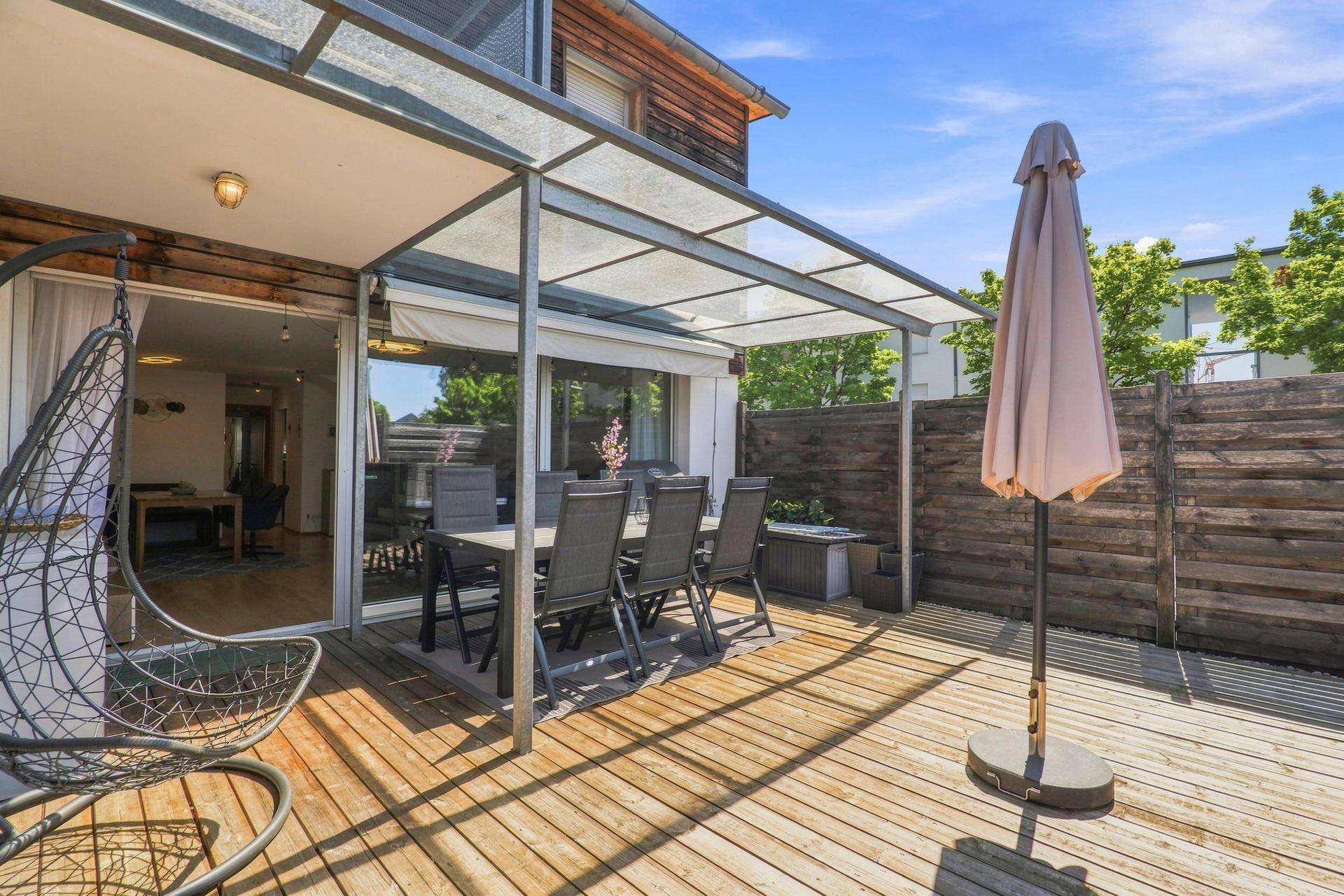 Sonnige Terrasse mit Überdachung, Essbereich und Hängesessel, ideal zum Entspannen.