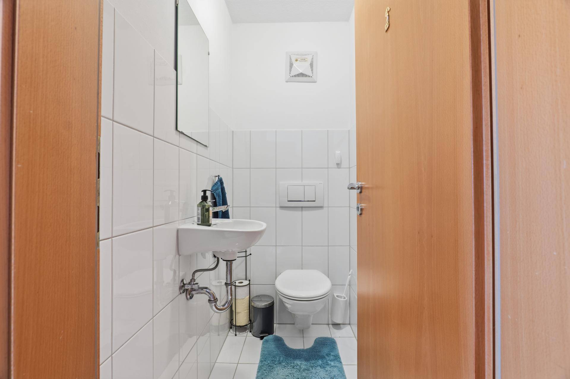 Separates Gäste-WC mit Waschbecken, Toilette und weiß gefliesten Wänden.