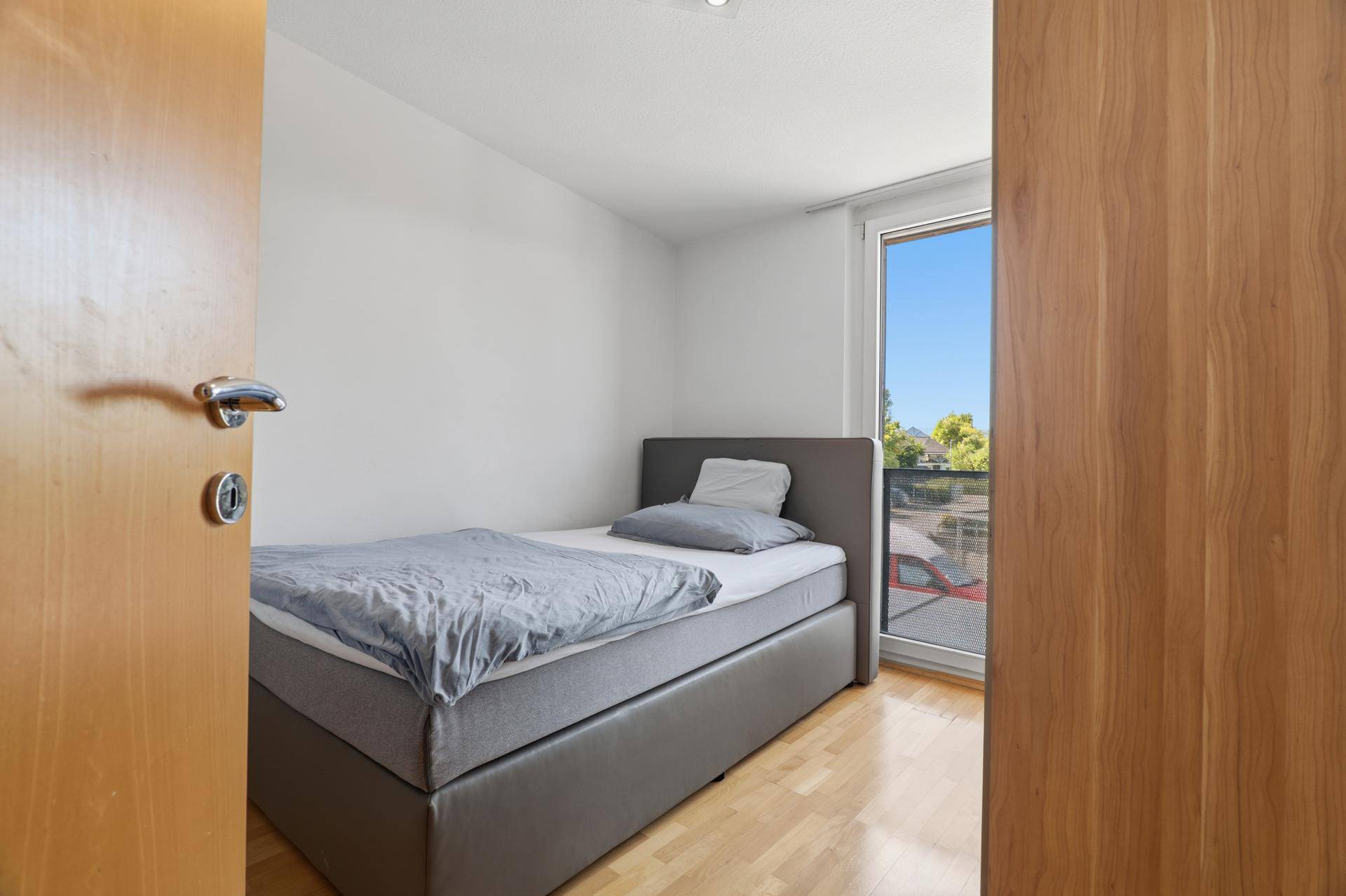 Kinderzimmer mit Einzelbett, Parkettboden und direktem Zugang zum Balkon.
