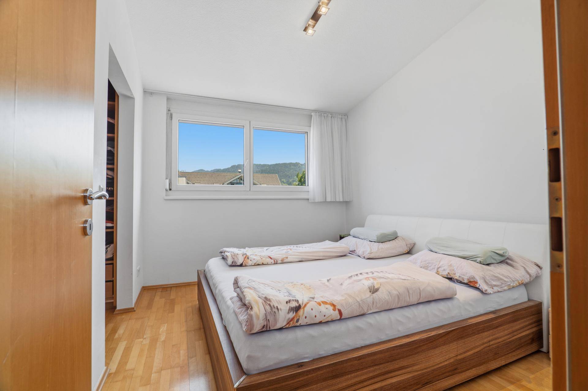 Schlafzimmer mit Holzbettrahmen, Parkettboden und einem schönen Blick ins Grüne.