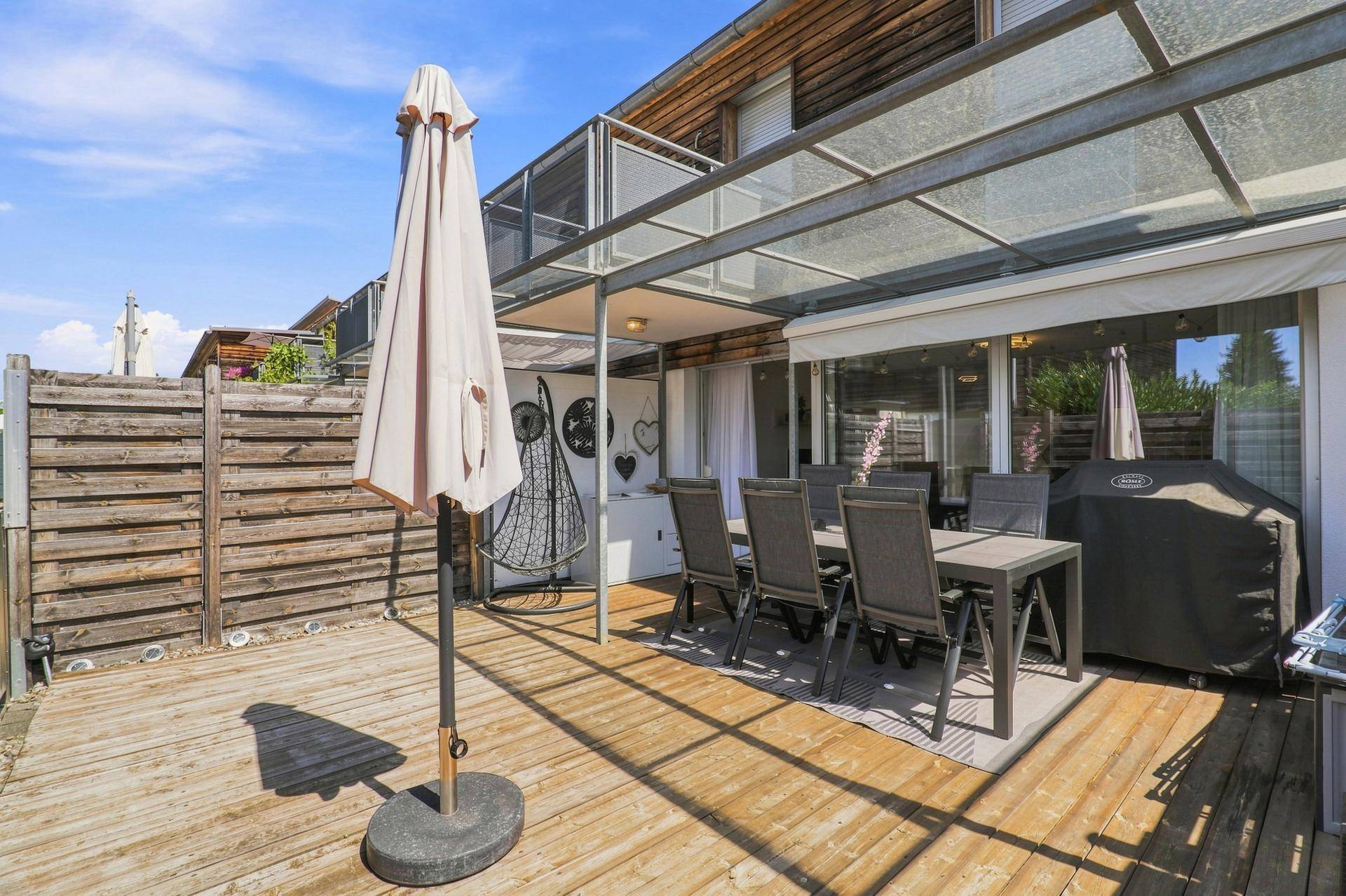 Geräumige Holzterrasse mit Essbereich, Sonnenschirm und Überdachung, ideal für Mahlzeiten im Freien.