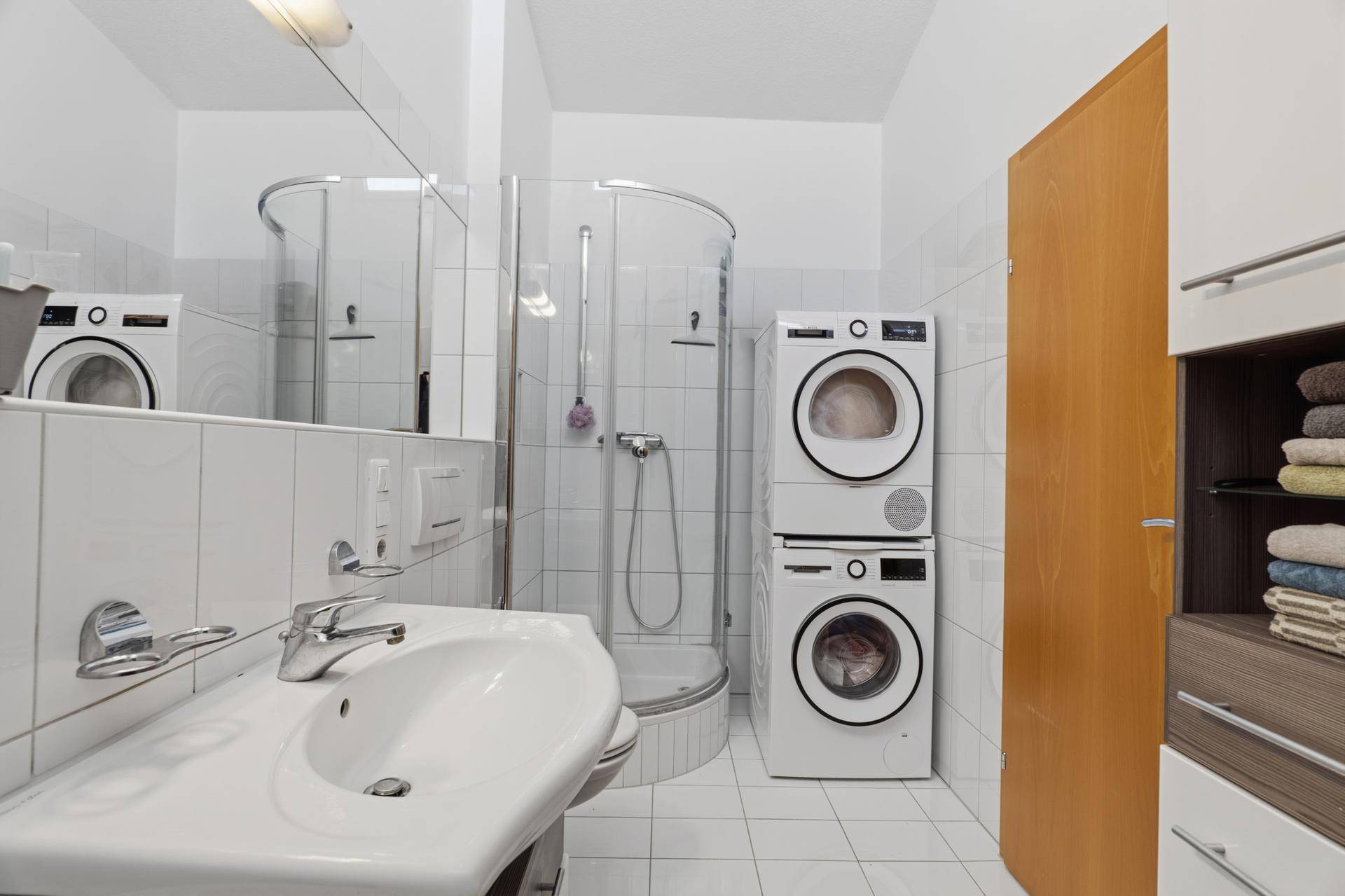 Badezimmer mit Duschkabine, Waschbecken und integriertem Waschmaschinen-Trockner-Turm.