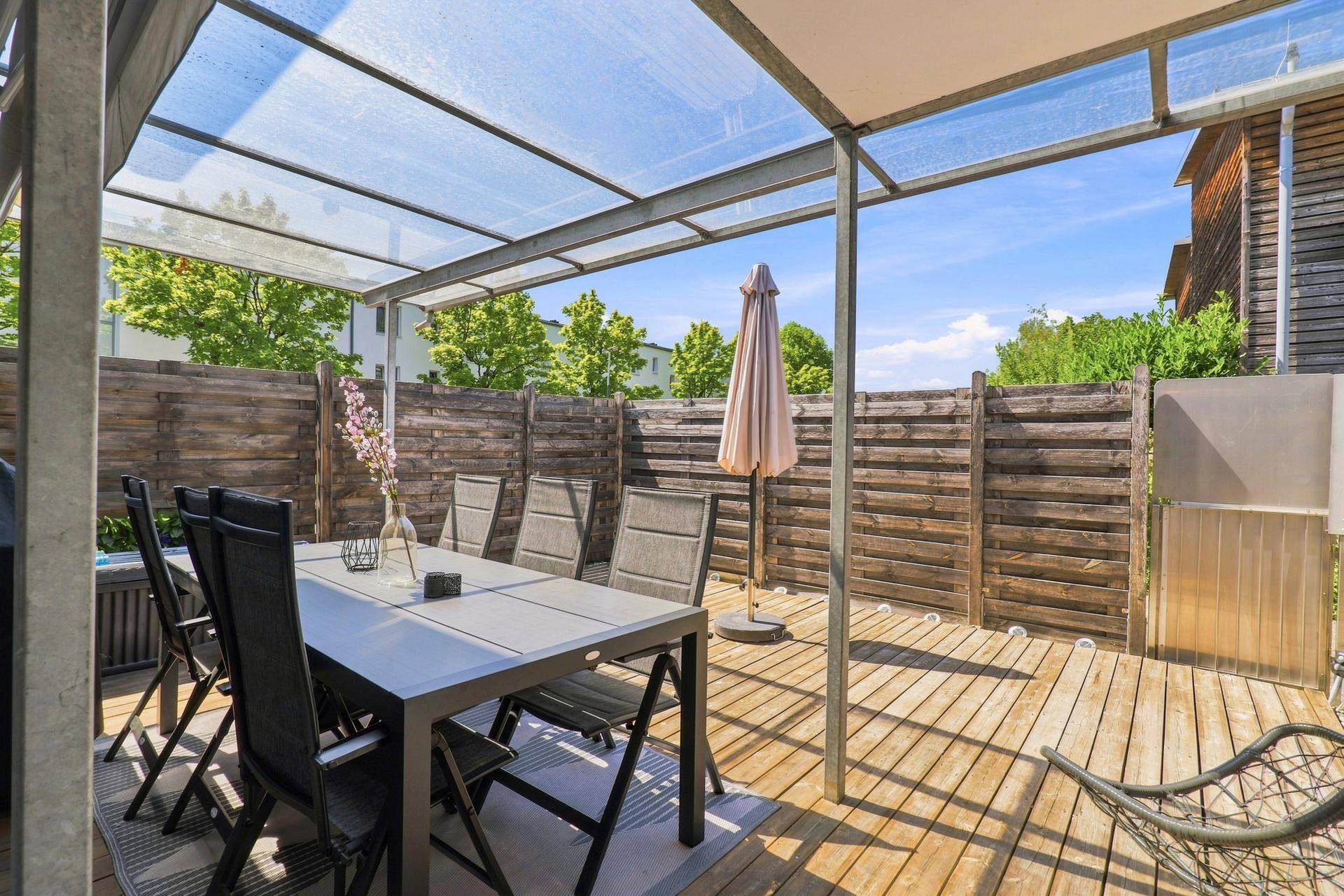 Überdachte Terrasse mit Esstisch und Stühlen, umgeben von einem Holzzaun.
