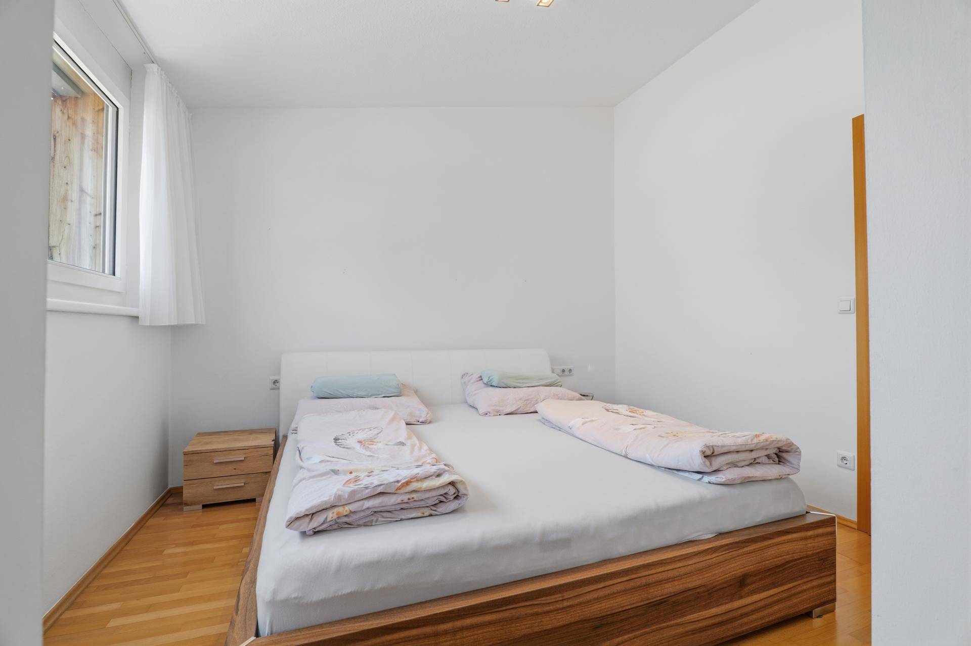 Helles Schlafzimmer mit Holzbett und Nachttisch, ausgestattet mit Parkettboden.