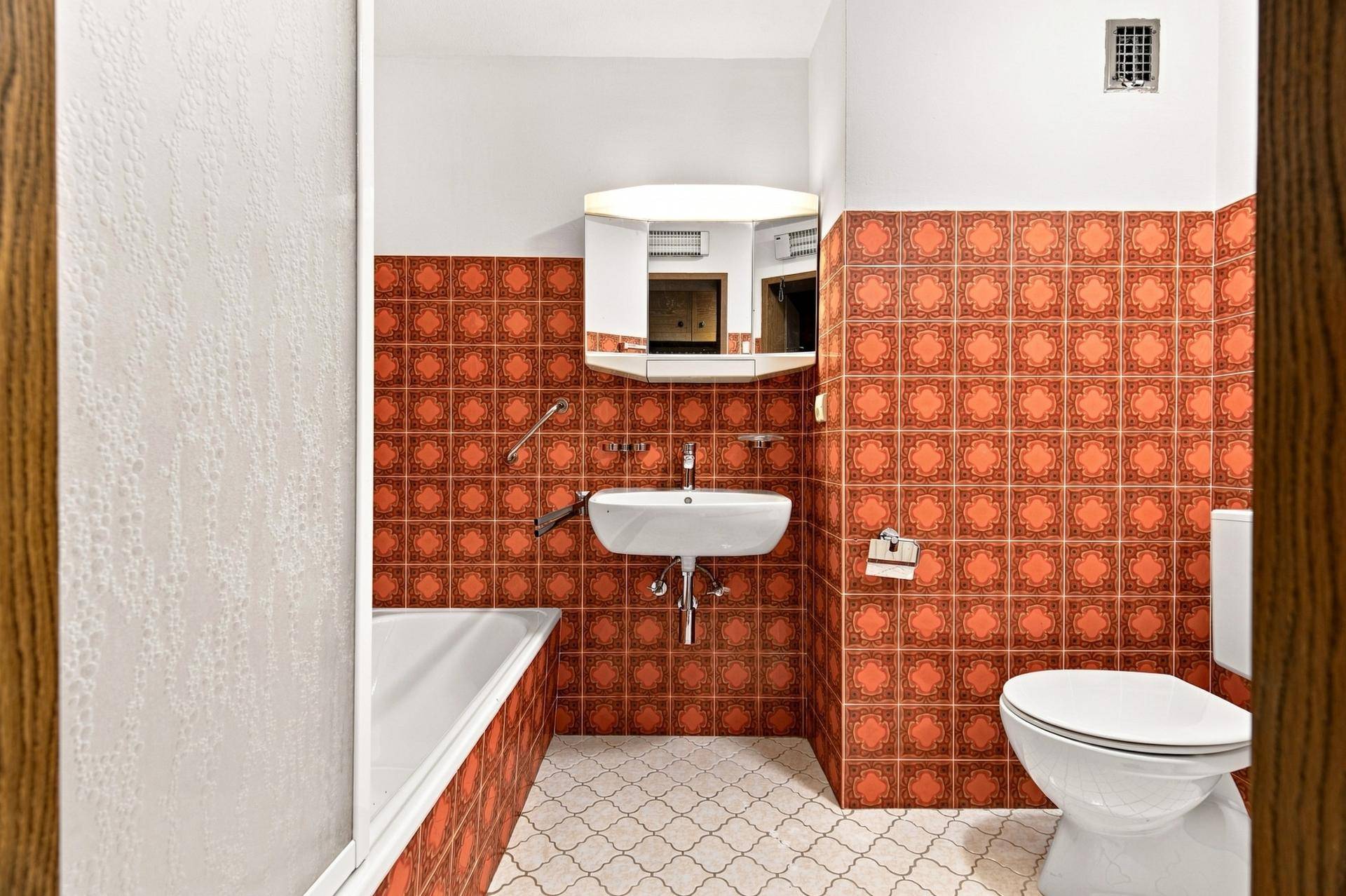 Badezimmer mit auffälligen orangefarbenen Fliesen, Badewanne, Waschbecken und Toilette, im Retro-Stil.