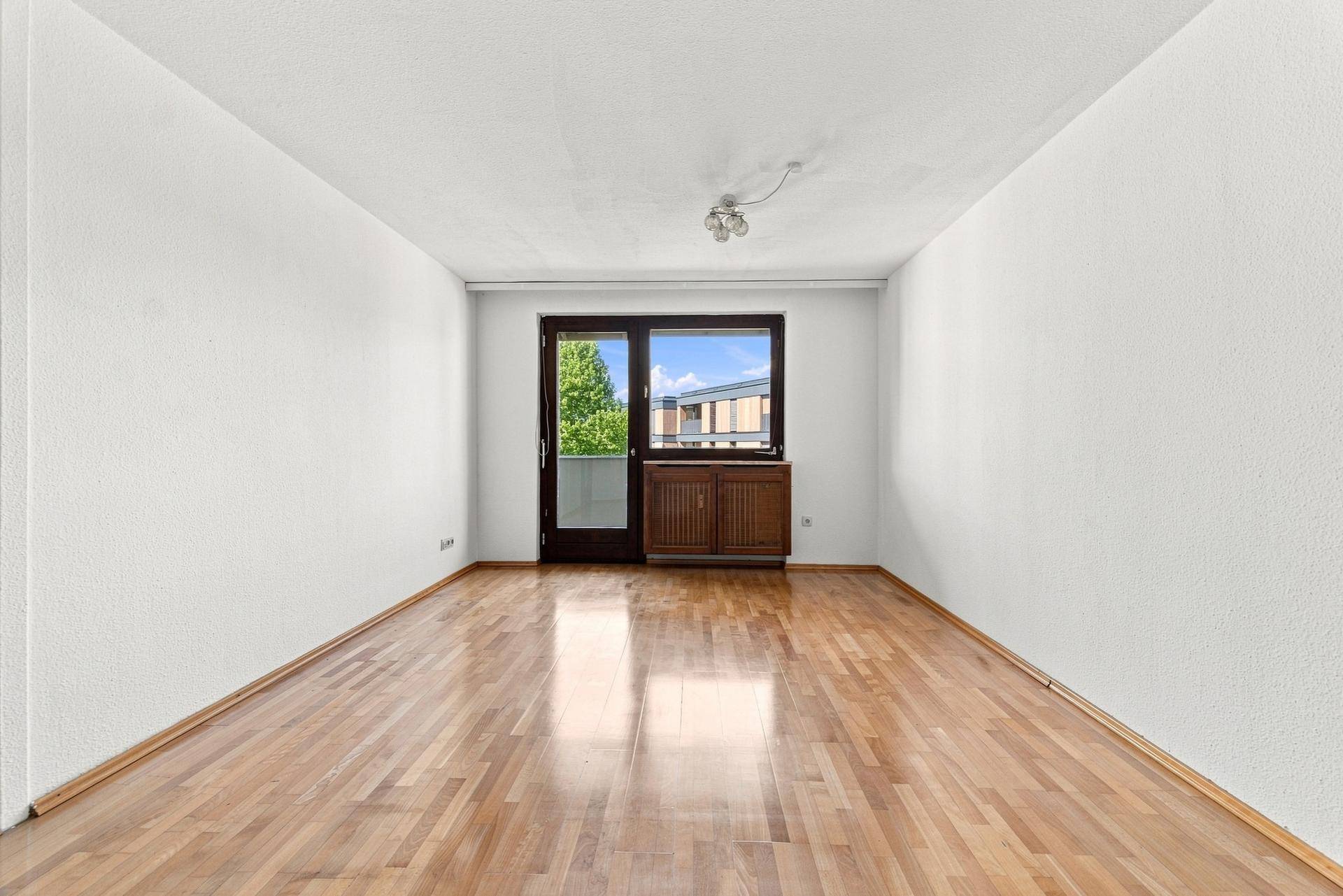 Geräumiges leeres Zimmer mit Holzboden und direktem Zugang zu einem sonnigen Balkon.