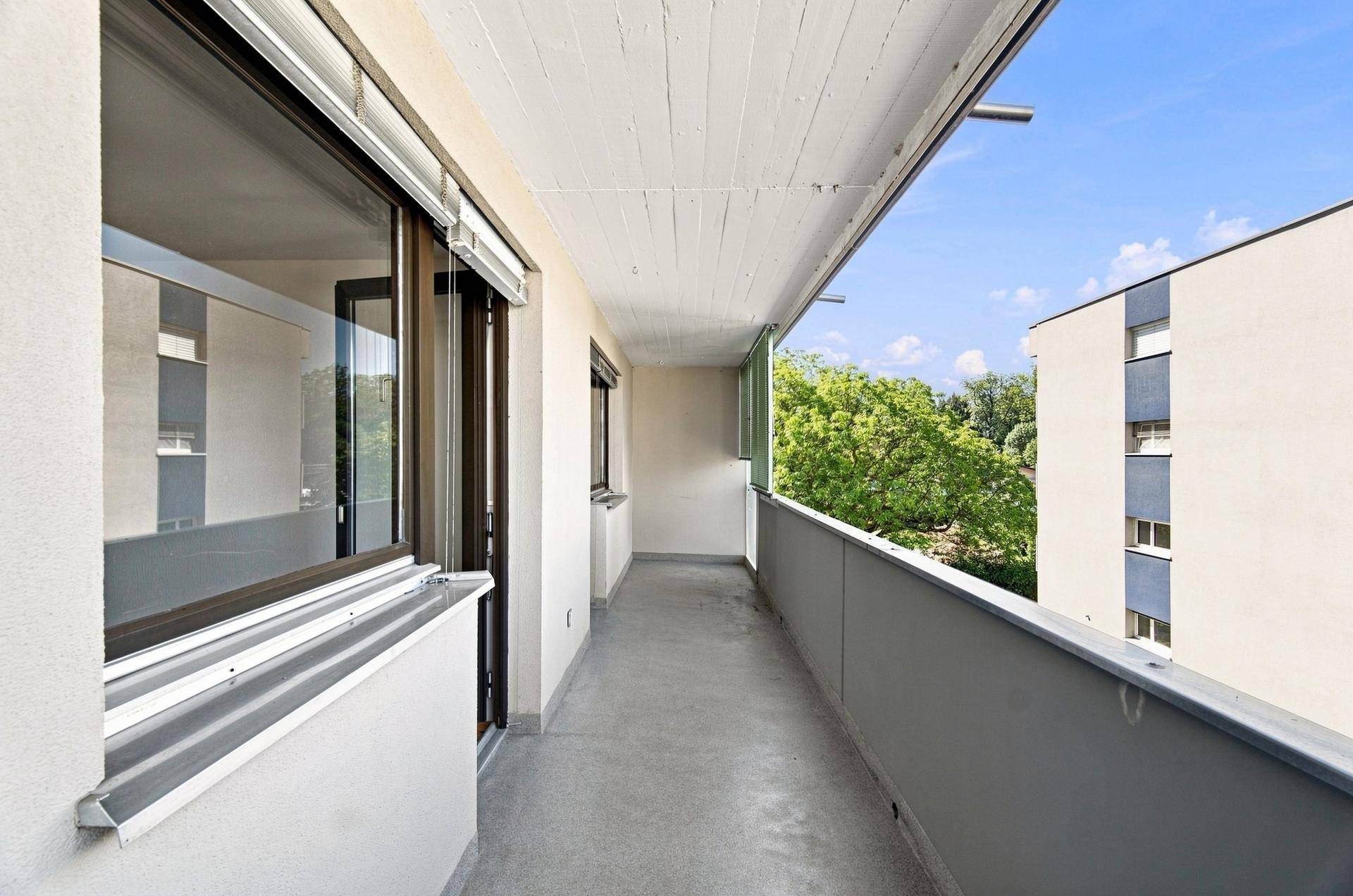 Langer Balkon mit weitem Blick auf die Nachbarschaft und viel Grün, bietet Entspannung im Freien.