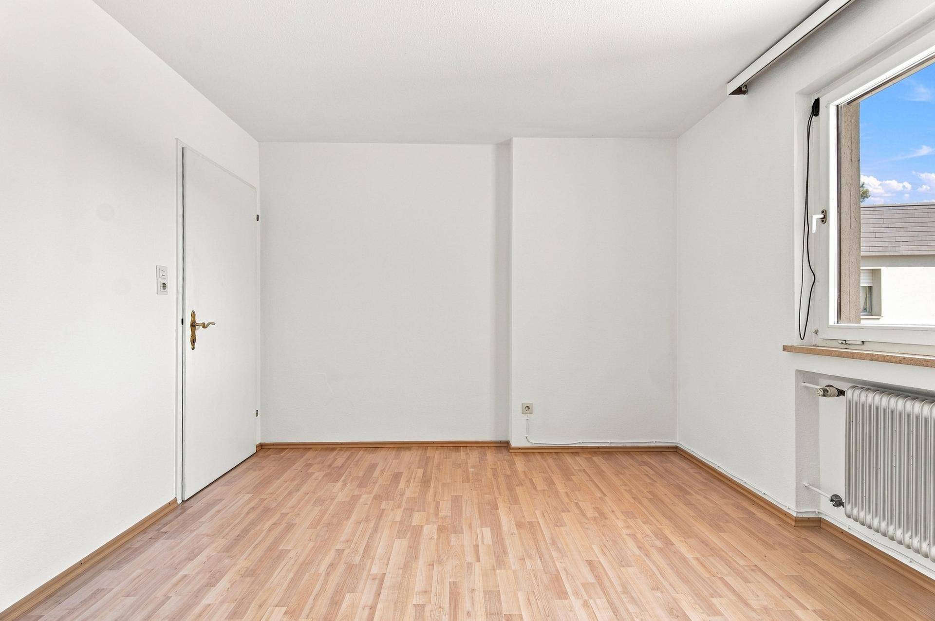Helles, leeres Zimmer mit Holzboden und Fenster, bereit zur individuellen Gestaltung und Nutzung.