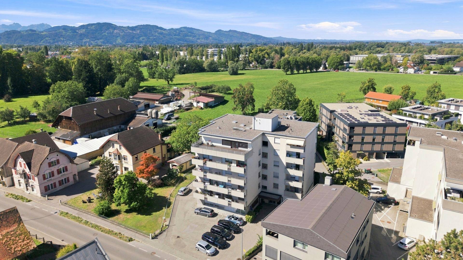 Weitläufige Luftaufnahme einer Wohnsiedlung mit grünen Wiesen und Bergen am Horizont, beeindruckende Landschaft.
