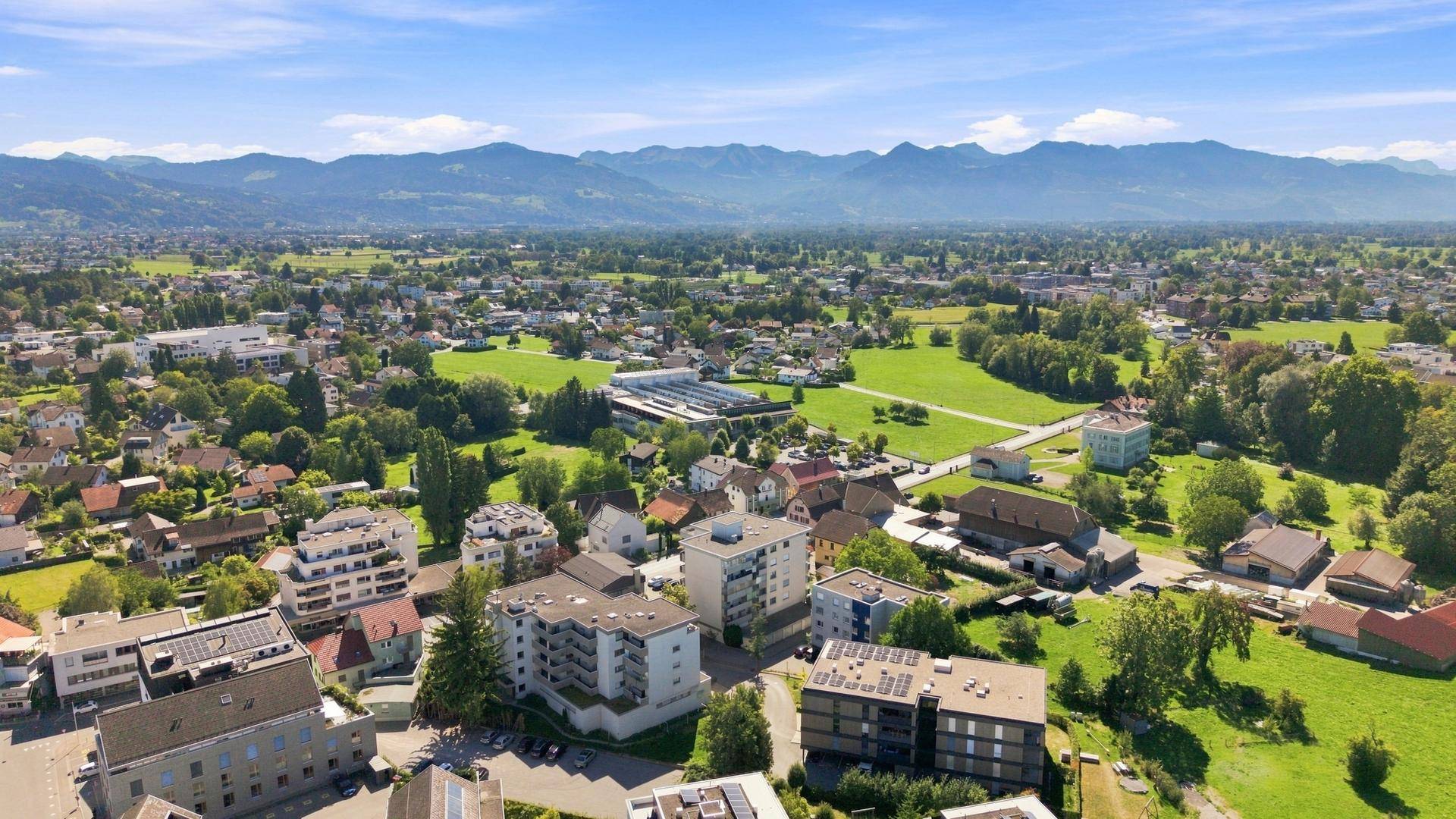 Panoramablick aus der Luft auf eine Wohngegend mit viel Grün und einer Bergkette, malerische Umgebung.