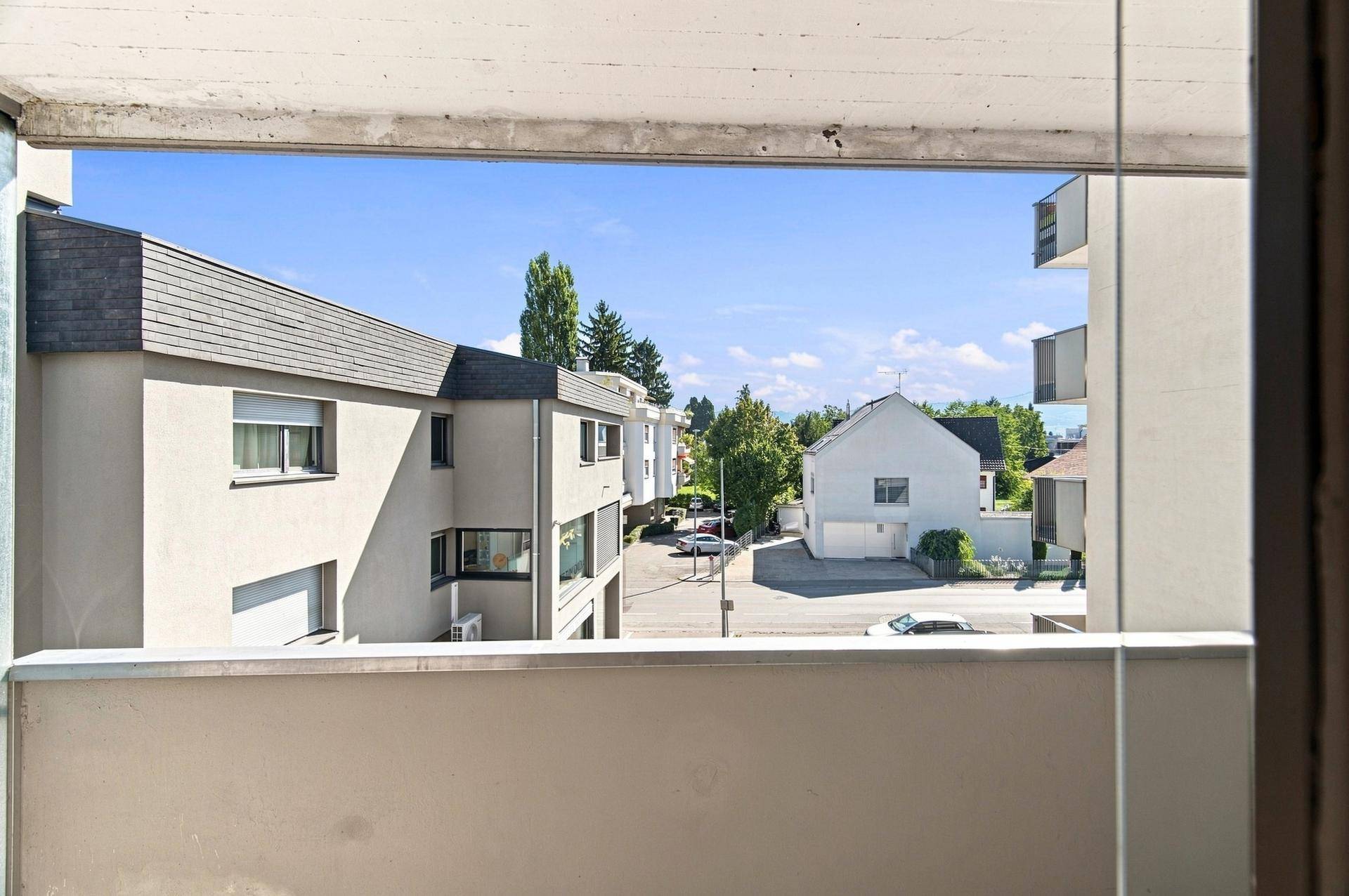 Ausblick vom Balkon auf die umliegenden Wohngebäude und grüne Bäume, eine ruhige Umgebung.