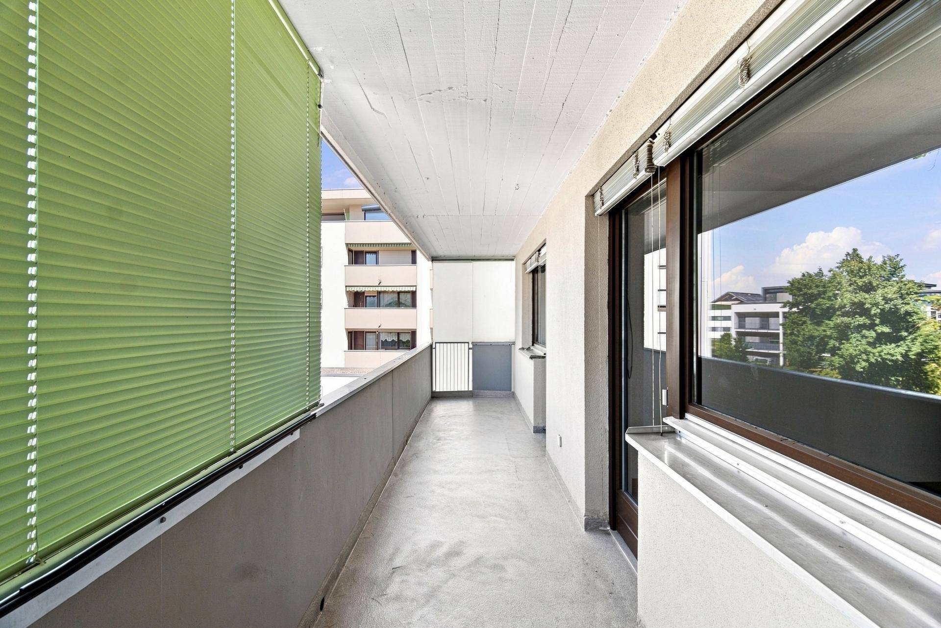 Geräumiger Balkon mit grüner Jalousie und Blick auf die umliegenden Gebäude, bietet Privatsphäre.