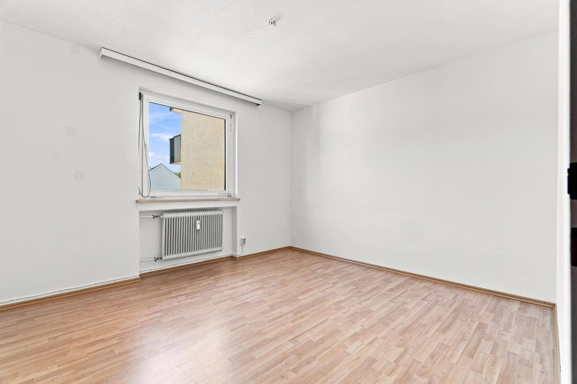 Leeres Zimmer mit Holzboden und großem Fenster, ideal als Kinder- oder Gästezimmer, vielseitig nutzbar.