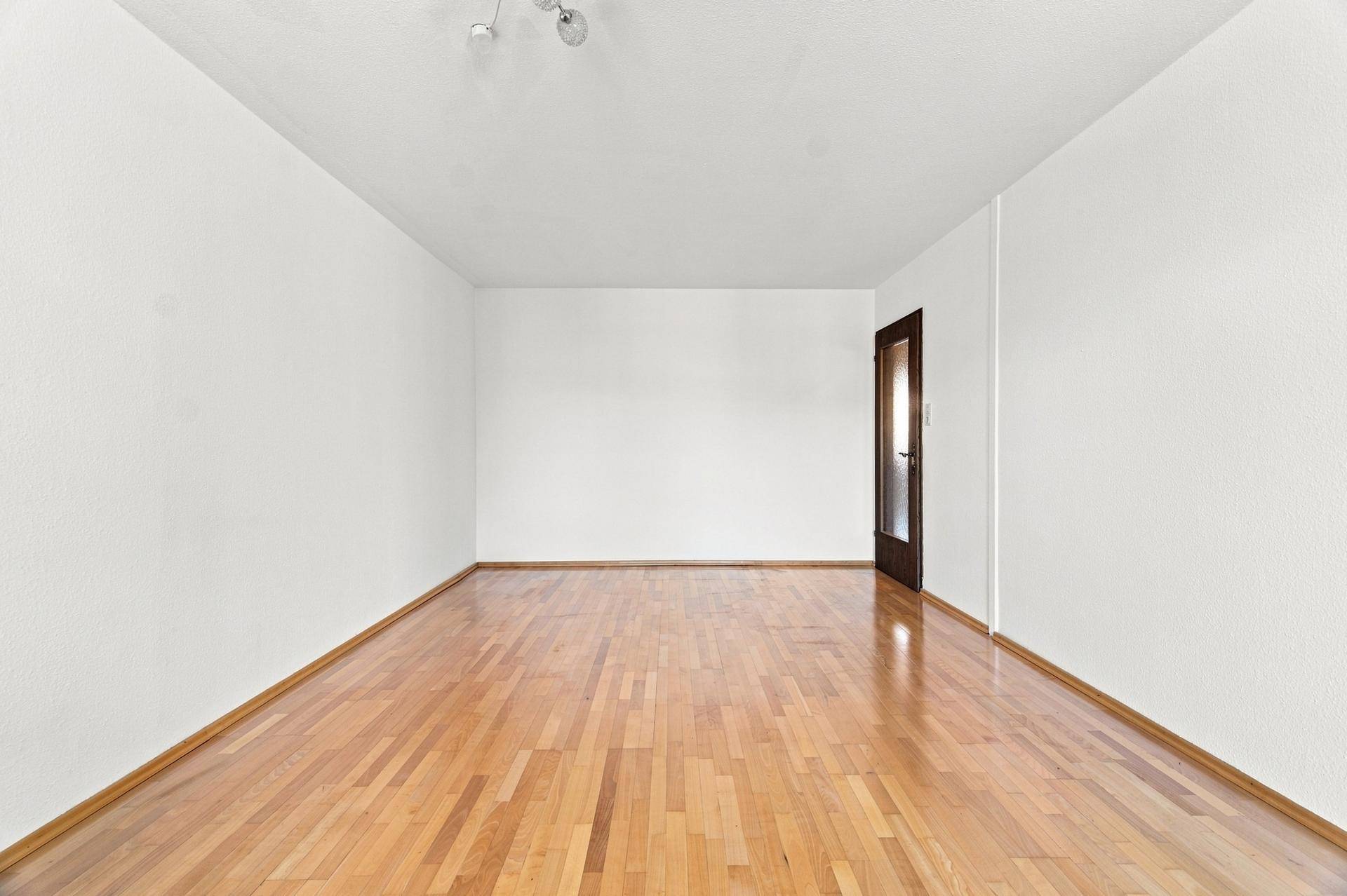 Leeres Zimmer mit glänzendem Holzboden und weiß gestrichenen Wänden, bereit zur Einrichtung.