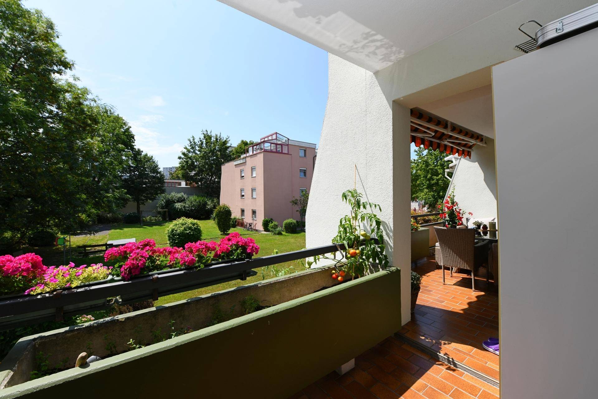 Heller Balkon mit Terrakotta-Fliesen, Blumenkästen und Blick auf den grünen Gartenbereich.