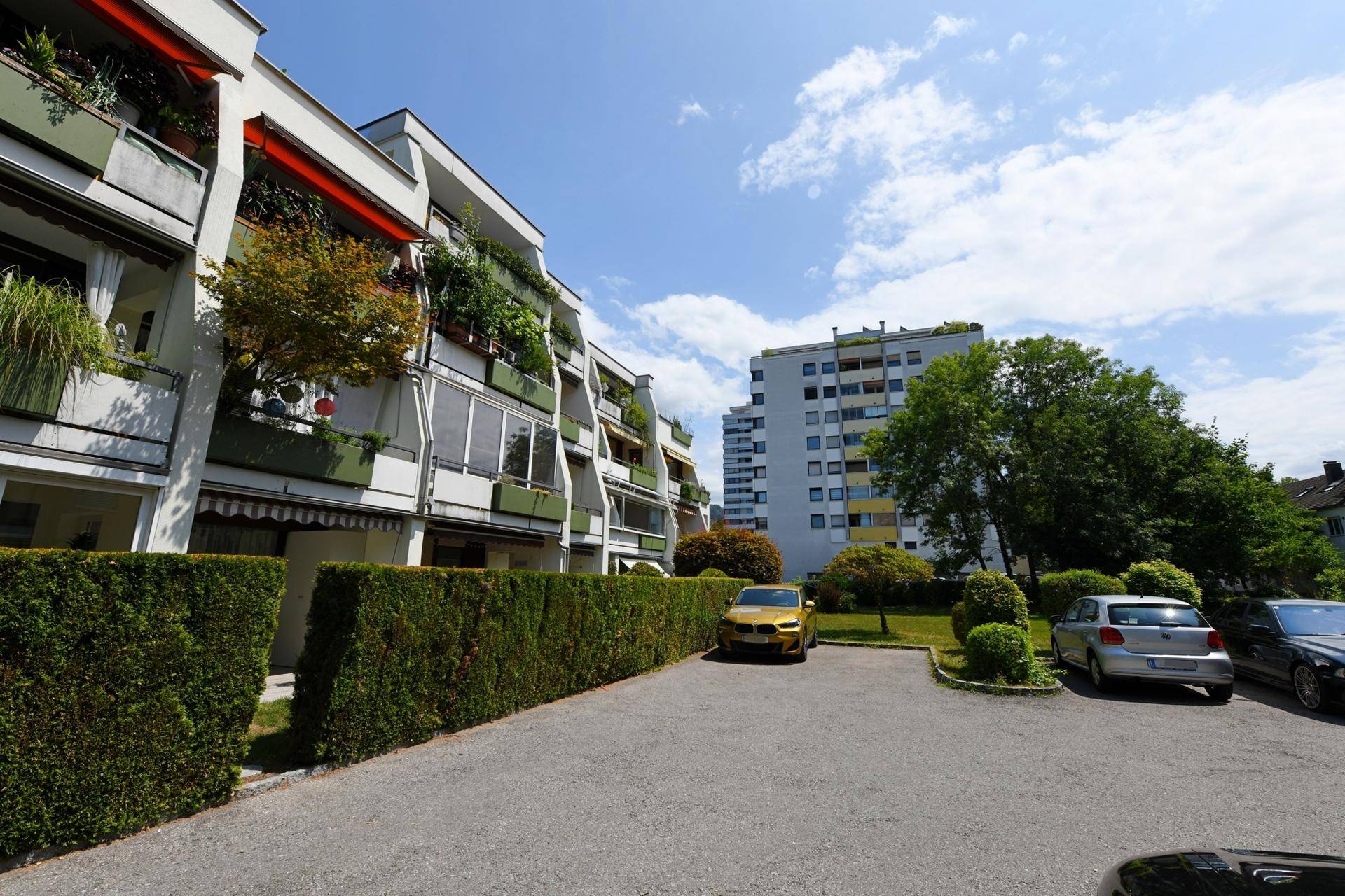 Moderne Wohnanlage mit begrünten Balkonen, gepflegter Hecke und Parkplätzen im Freien.