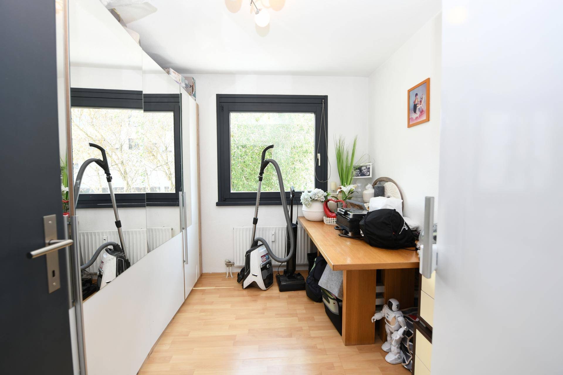 Funktionales Zimmer mit Schreibtisch, Spiegelschrank und Holzboden, ideal als Büro oder Kinderzimmer.