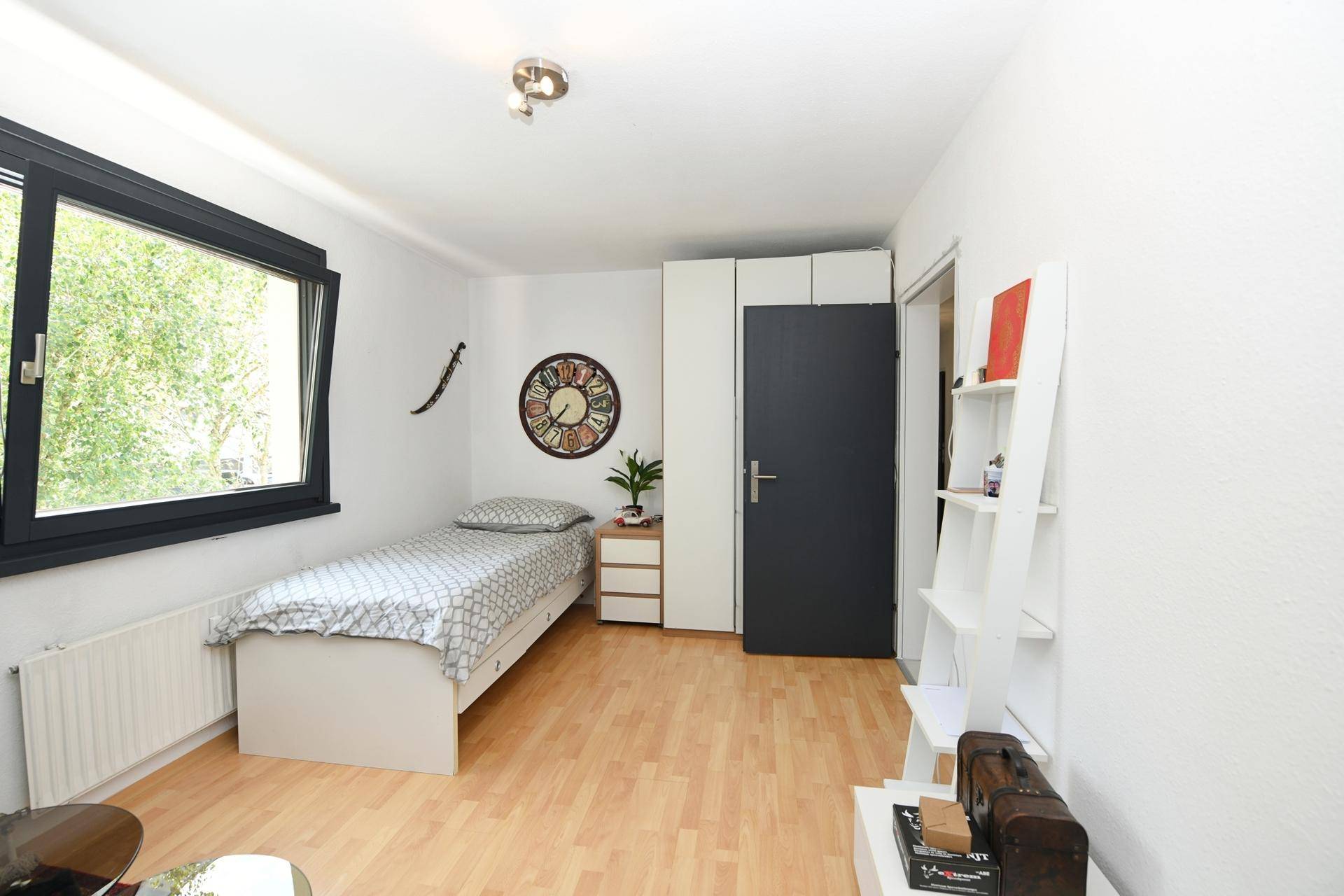 Helles Kinderzimmer mit Einzelbett, Kleiderschrank und Holzboden.