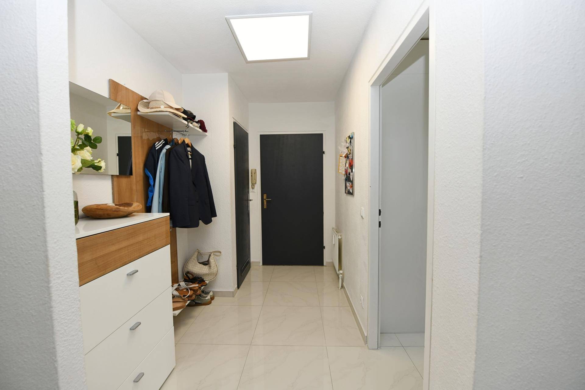 Eingangsbereich mit Garderobe, Schuhschrank und hellen Fliesen.