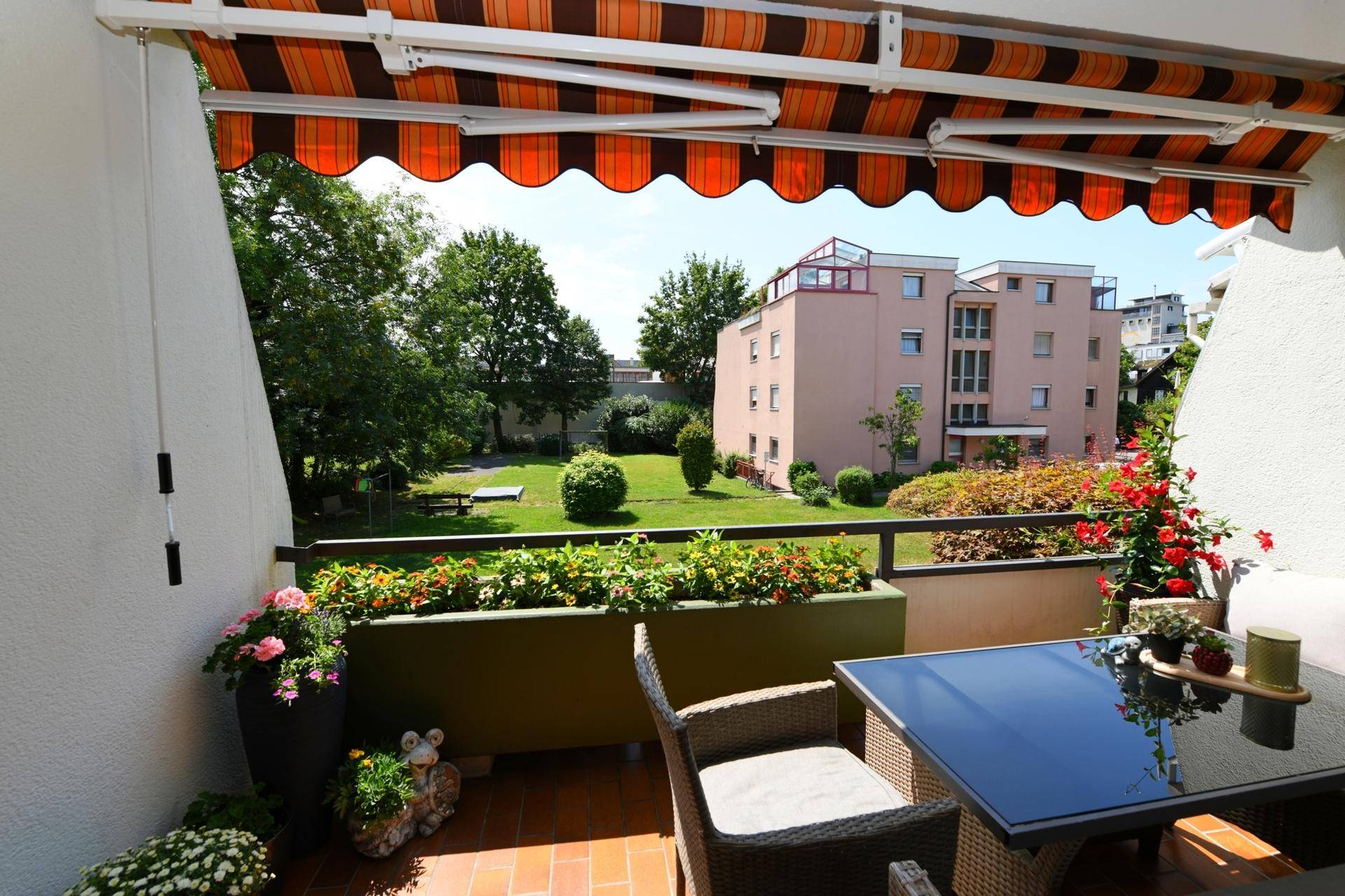 Möblierter Balkon mit Markise und Blick auf die grüne Gemeinschaftsanlage.