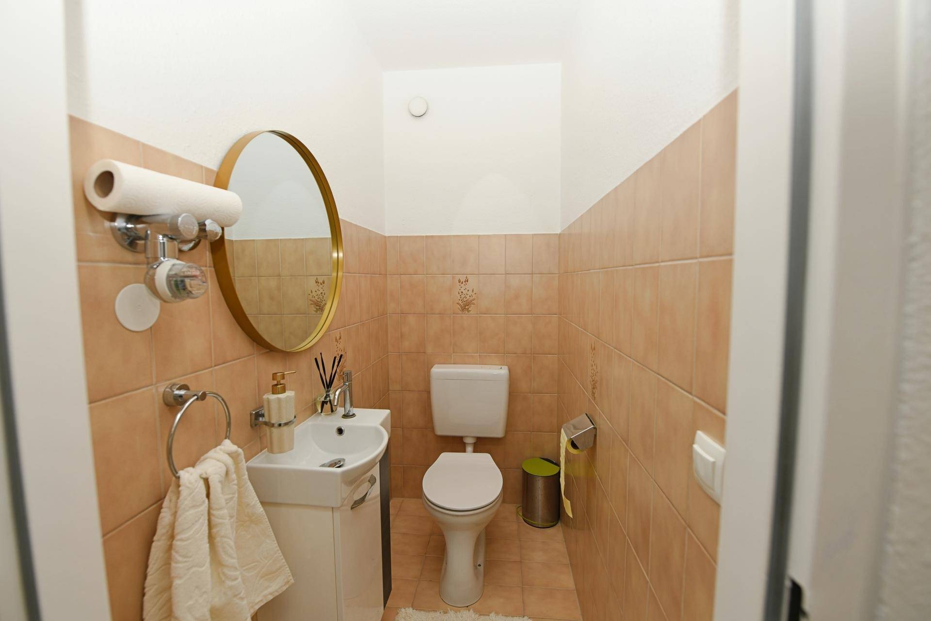 Kleines Gäste-WC mit Waschbecken, Toilette und beigefarbenen Fliesen.