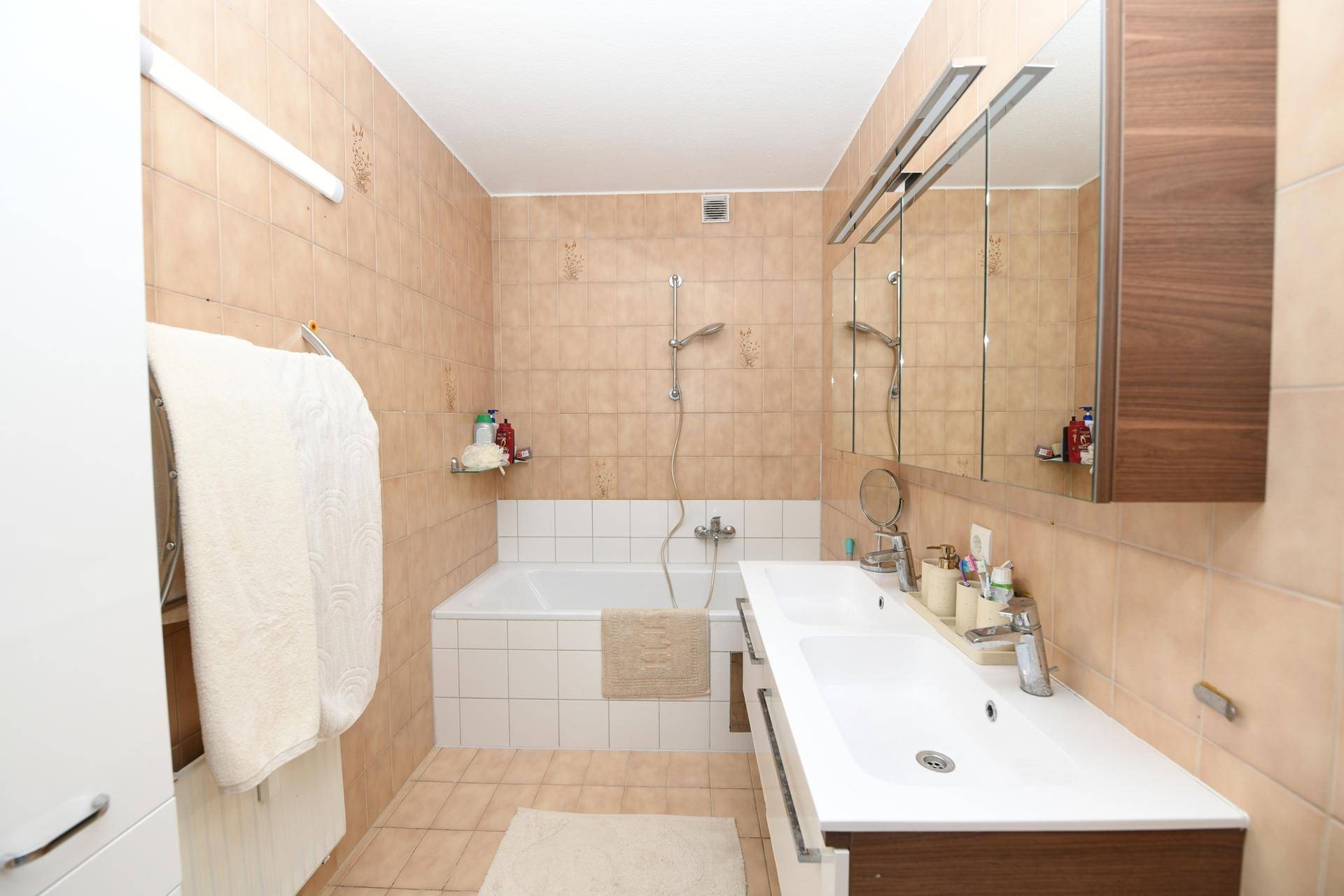 Geräumiges Badezimmer mit Badewanne, Doppelwaschbecken und beigefarbenen Fliesen.