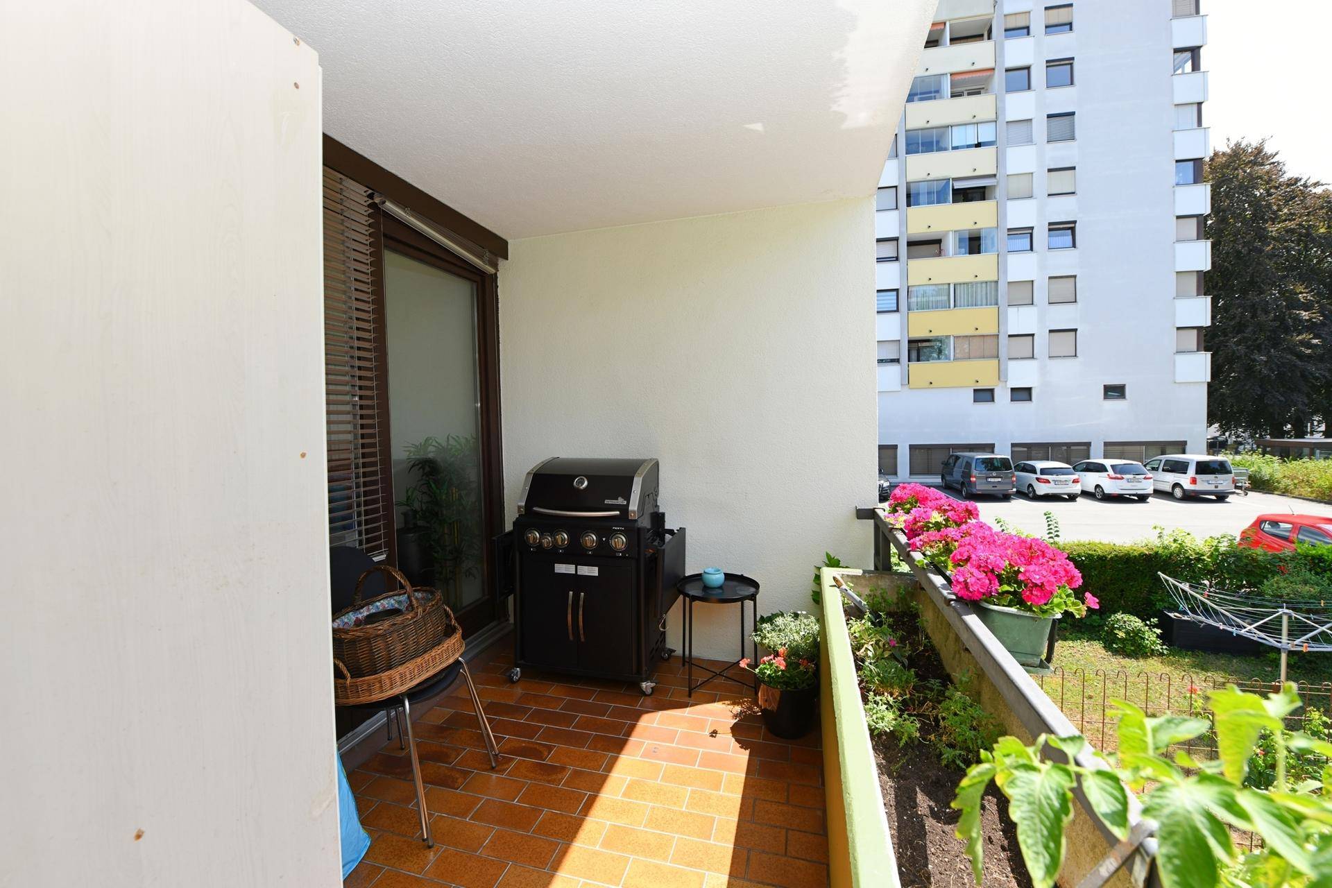 Sonnenverwöhnter Balkon mit Gasgrill, Blumenkästen und Blick auf die umliegenden Gebäude.