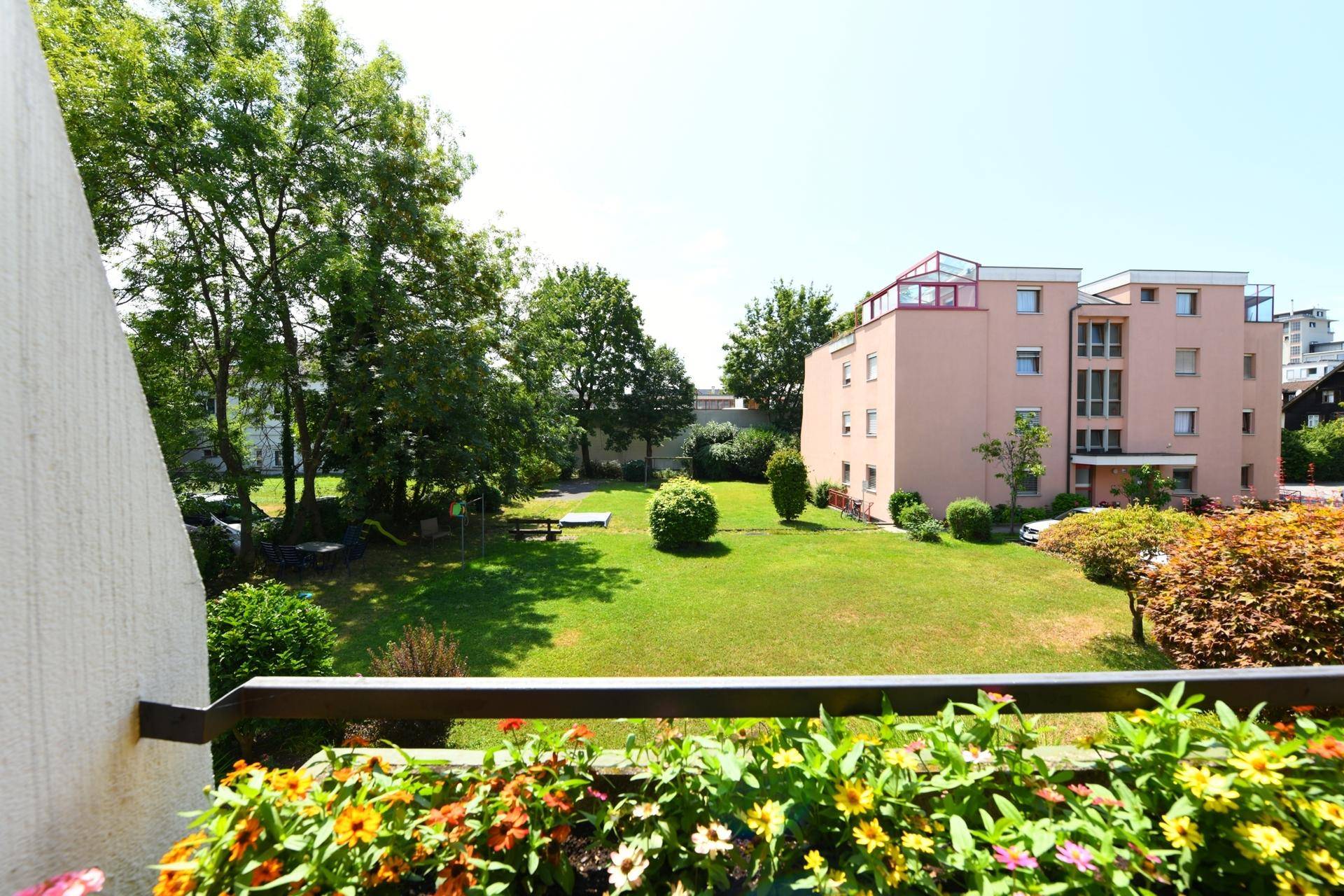 Weitläufiger Blick vom Balkon auf eine gepflegte Grünanlage mit Bäumen und Spielplatz.