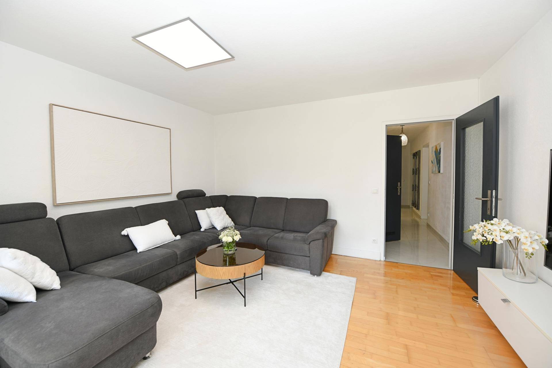 Heller Wohnbereich mit gemütlicher Eckcouch und Blick in den angrenzenden Flur der Wohnung.