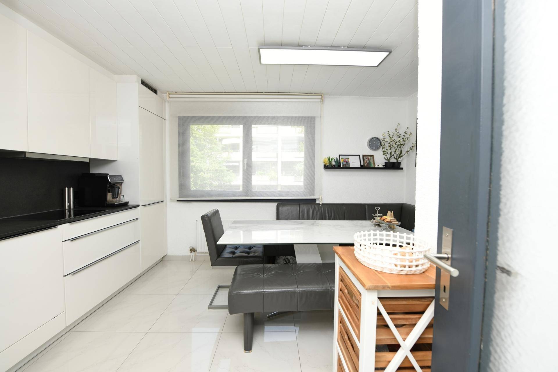 Moderne Wohnküche mit weißen Hochglanzschränken, Essbereich und großem Fenster für Tageslicht.