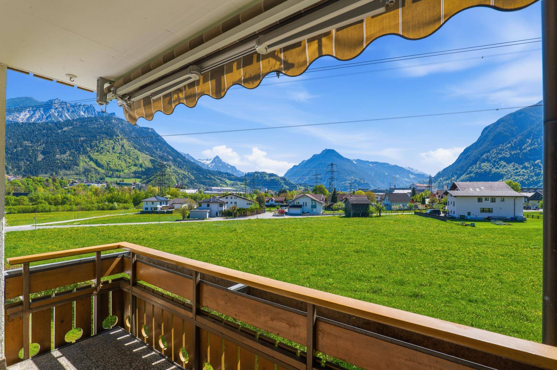 Breiter Balkon mit Markise und atemberaubendem Panoramablick auf die Alpen und das Tal.