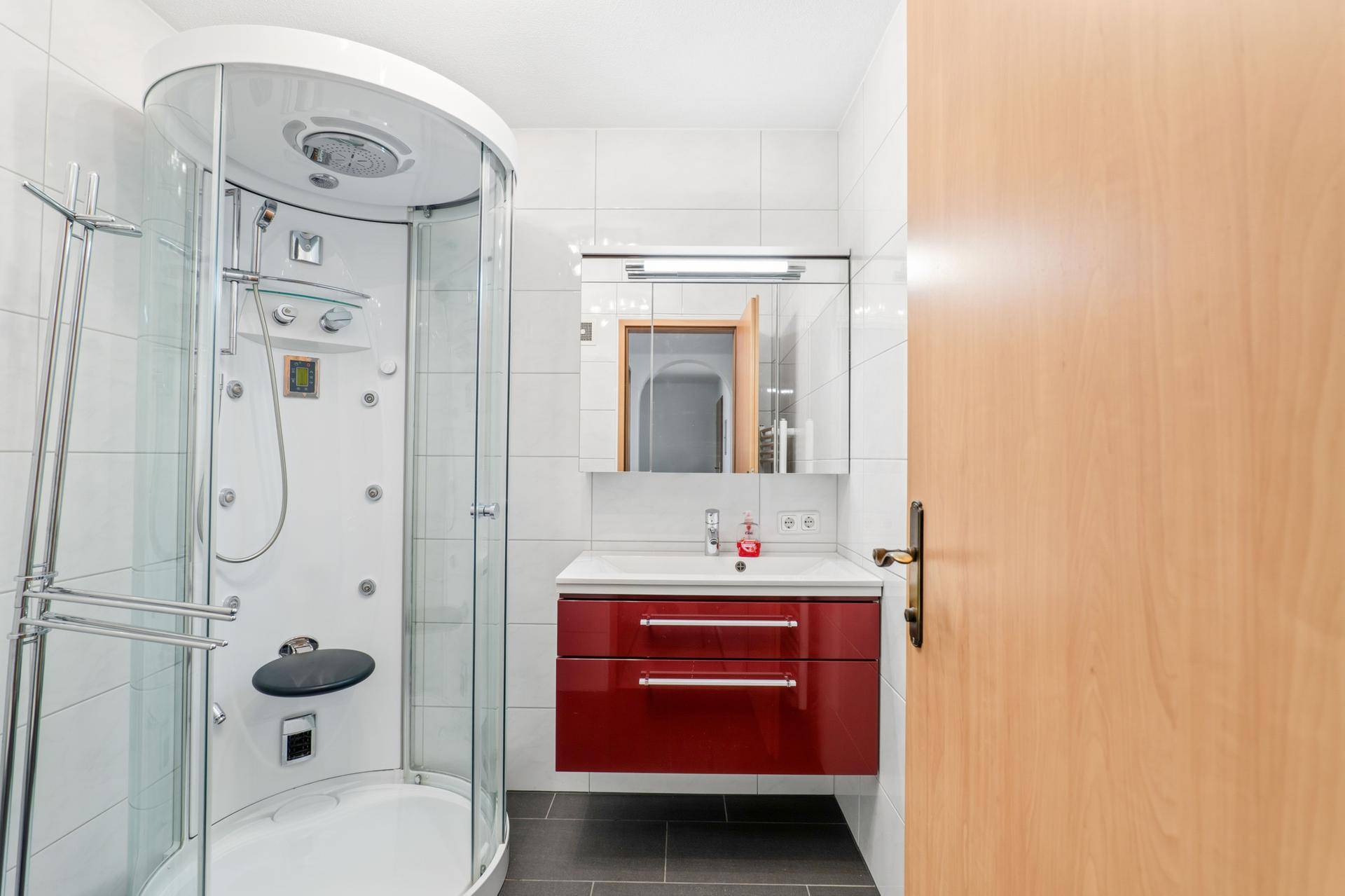 Modernes Badezimmer mit Duschkabine, rotem Waschtischunterschrank und weißen Fliesen.