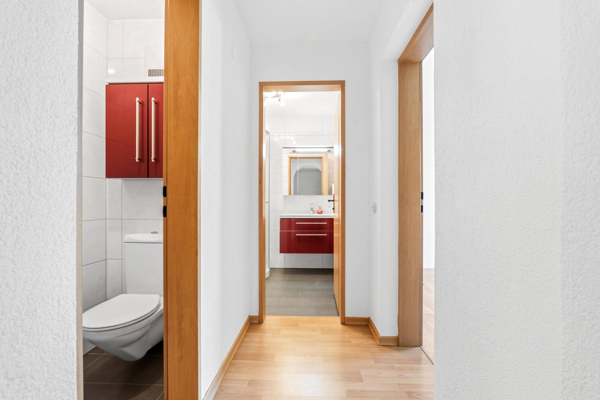 Separates WC mit wandhängender Toilette, roten Hängeschränken und Holztür.