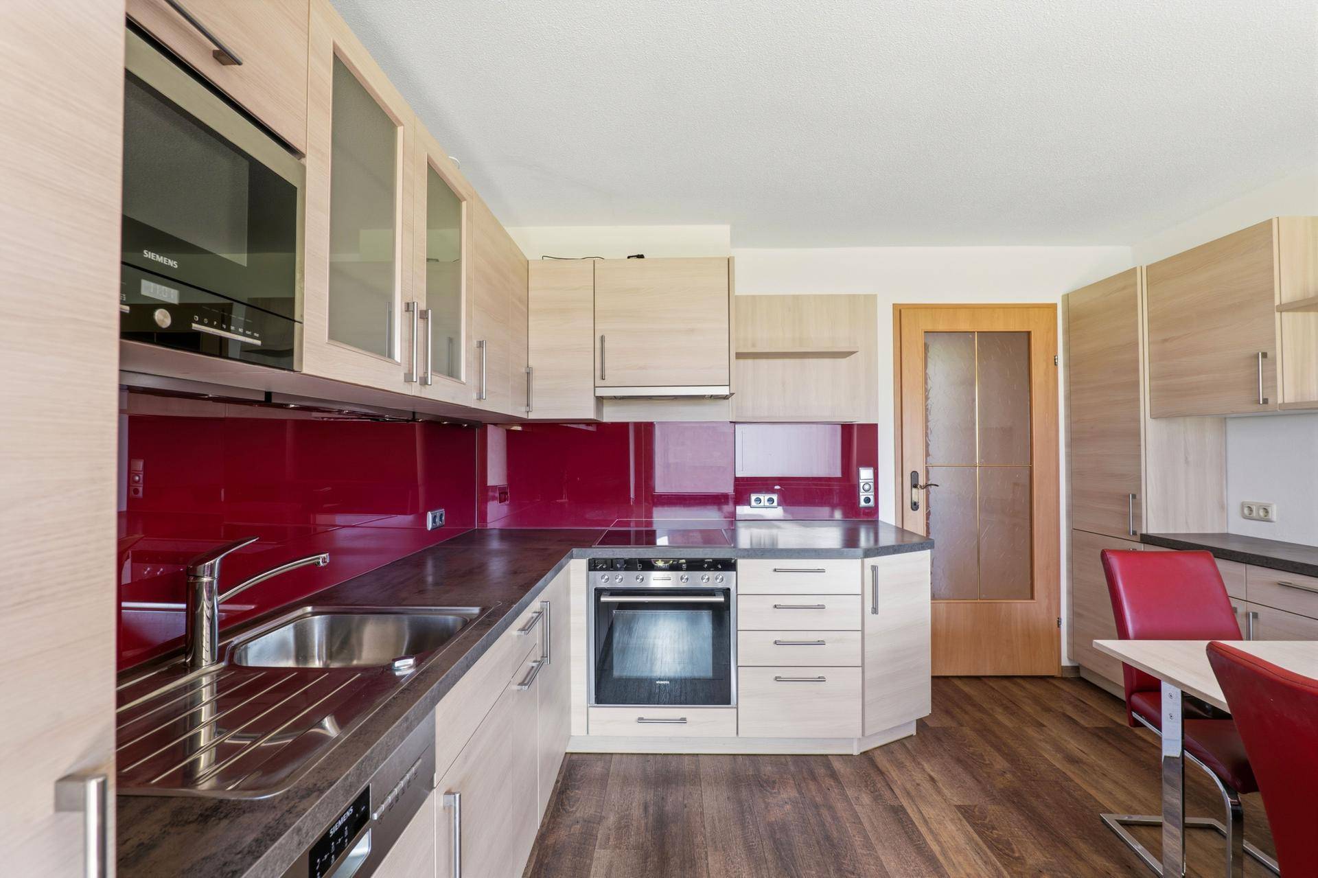 Moderne Einbauküche mit hellen Holzfronten, roter Rückwand und integrierten Siemens-Geräten.