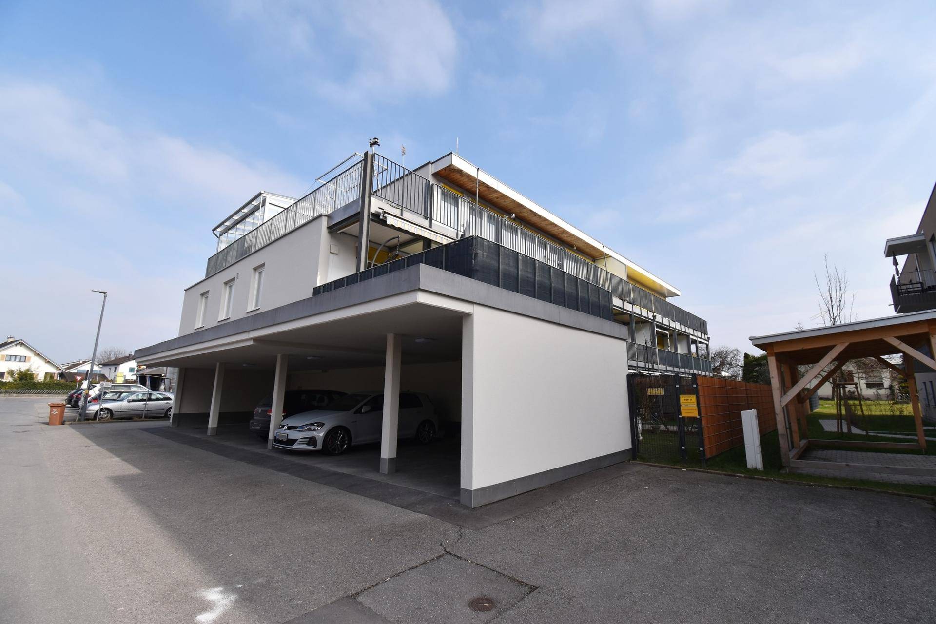 Modernes Mehrfamilienhaus mit Carport-Parkplätzen und Balkonen.