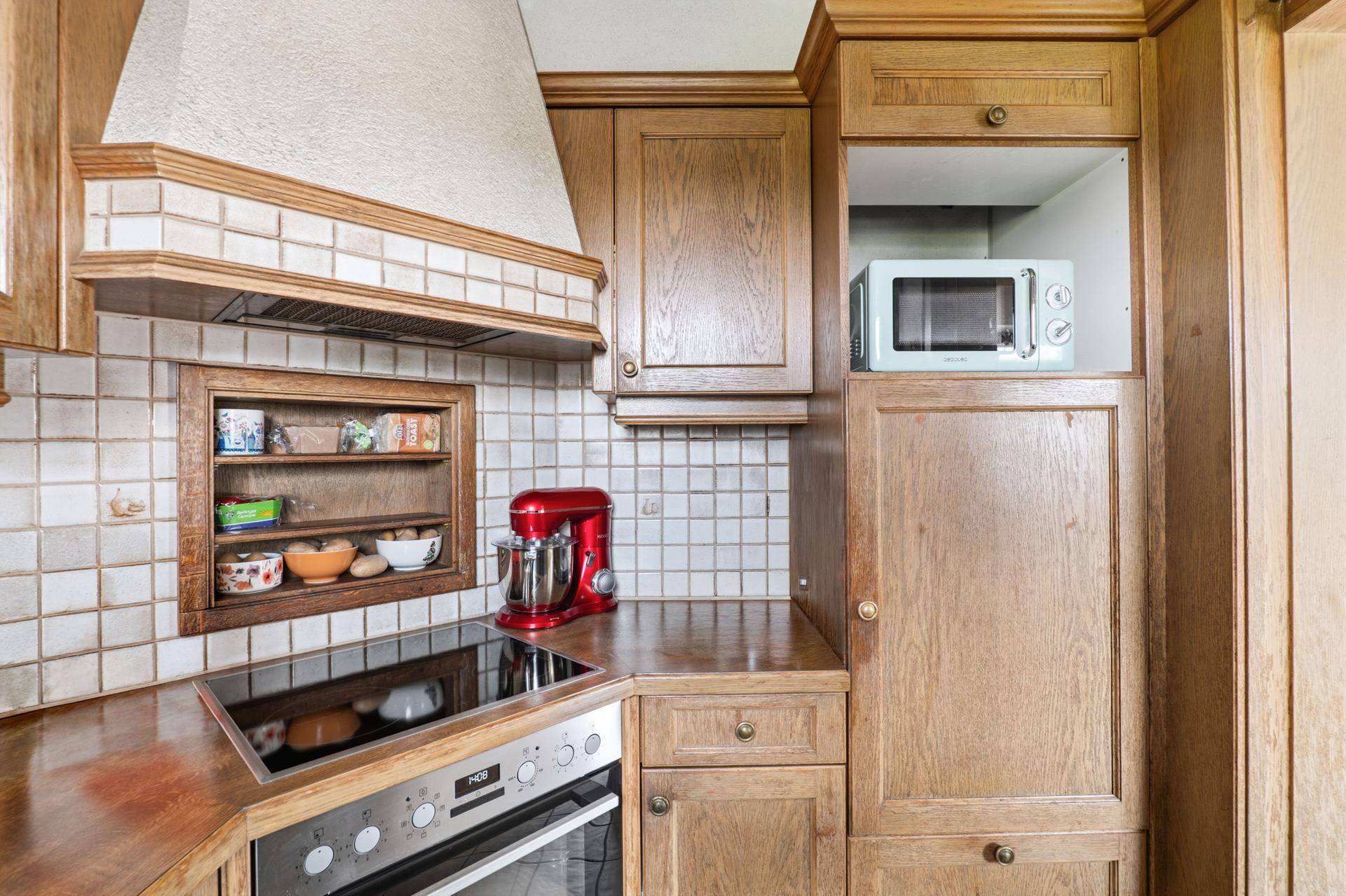 Detailansicht der Holzküche mit Kochfeld, Backofen und integrierter Mikrowelle.