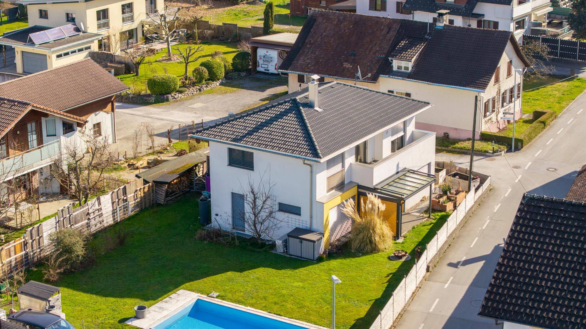 Luftaufnahme eines Einfamilienhauses mit Garten, Pool und angrenzender Straße in sonniger Lage.