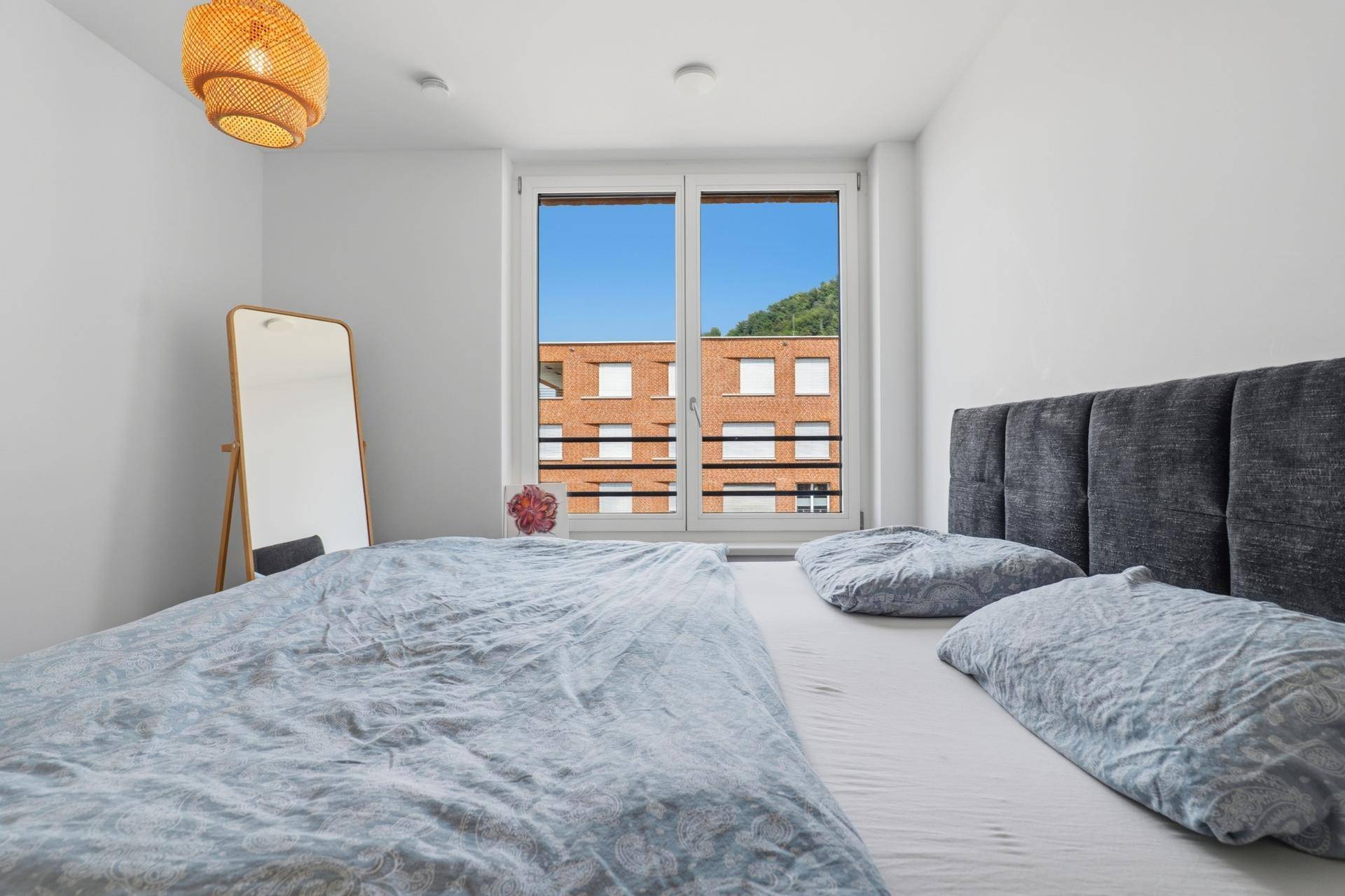 Schlafzimmer mit bequemen Doppelbett und Fenster, das einen Blick auf die umliegenden Gebäude bietet.