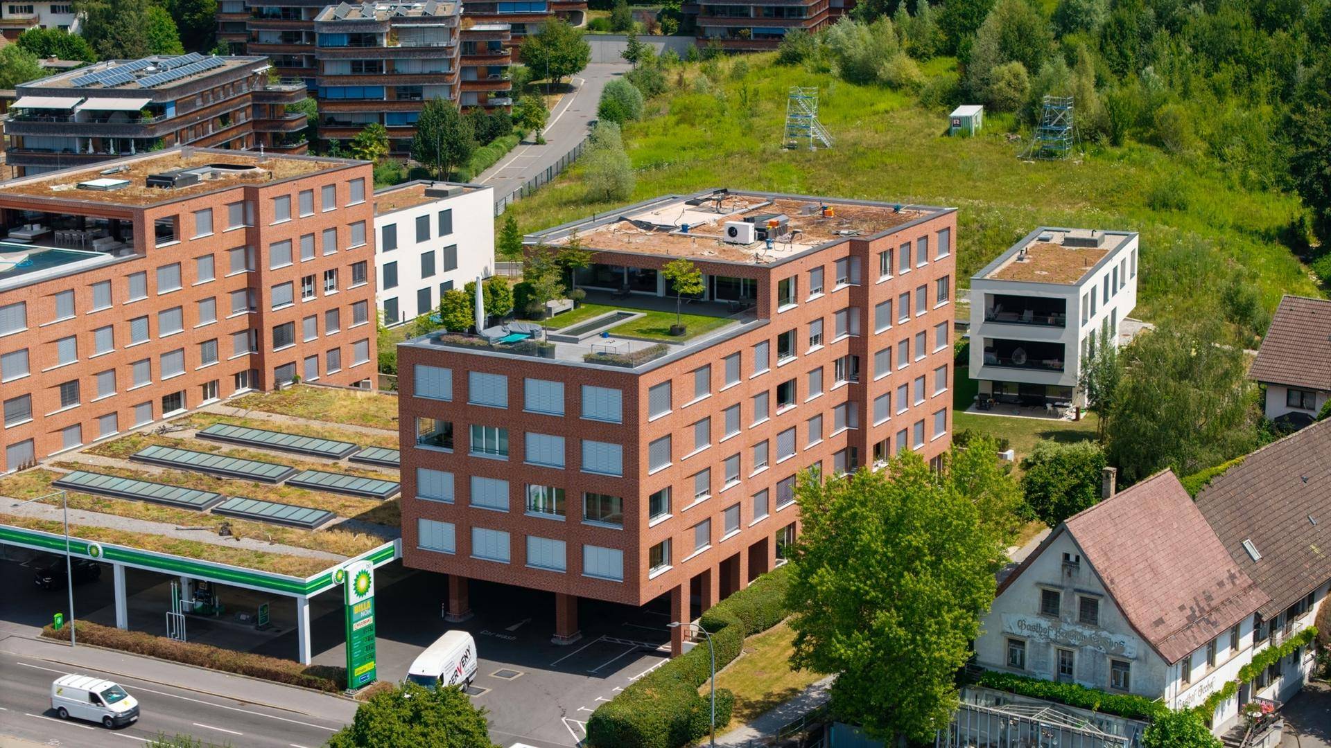Luftaufnahme moderner Gebäude mit begrünten Dächern und Photovoltaikanlagen in grüner Umgebung.