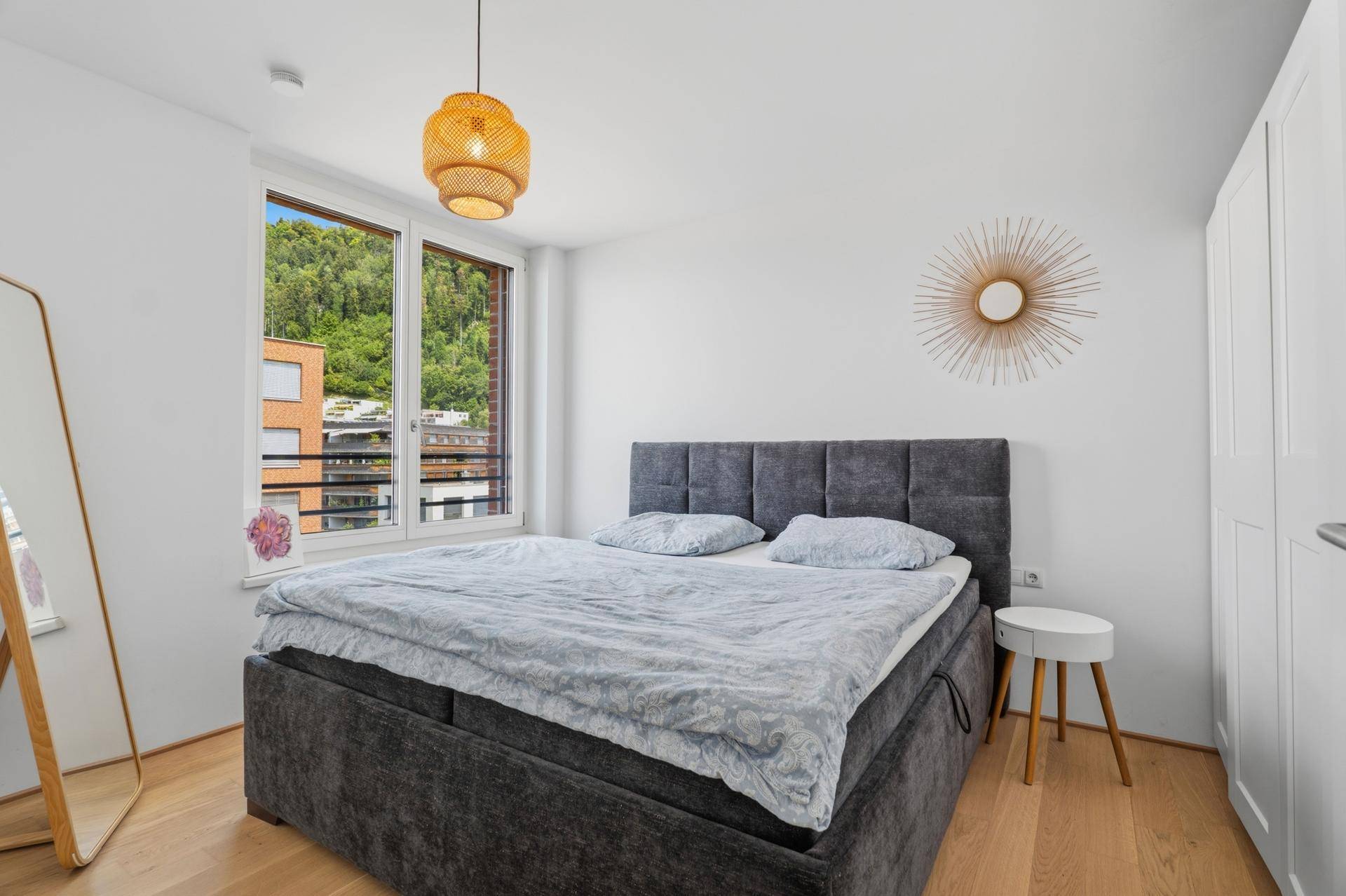 Helles Schlafzimmer mit Doppelbett, Holzboden und Fenster mit Blick ins Grüne.