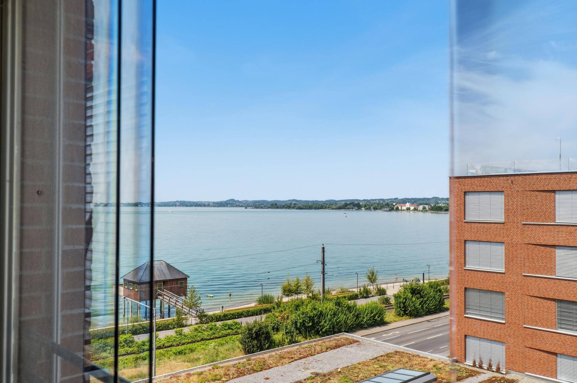 Weitläufiger Seeblick aus dem Fenster, umgeben von Gebäuden und grüner Landschaft.