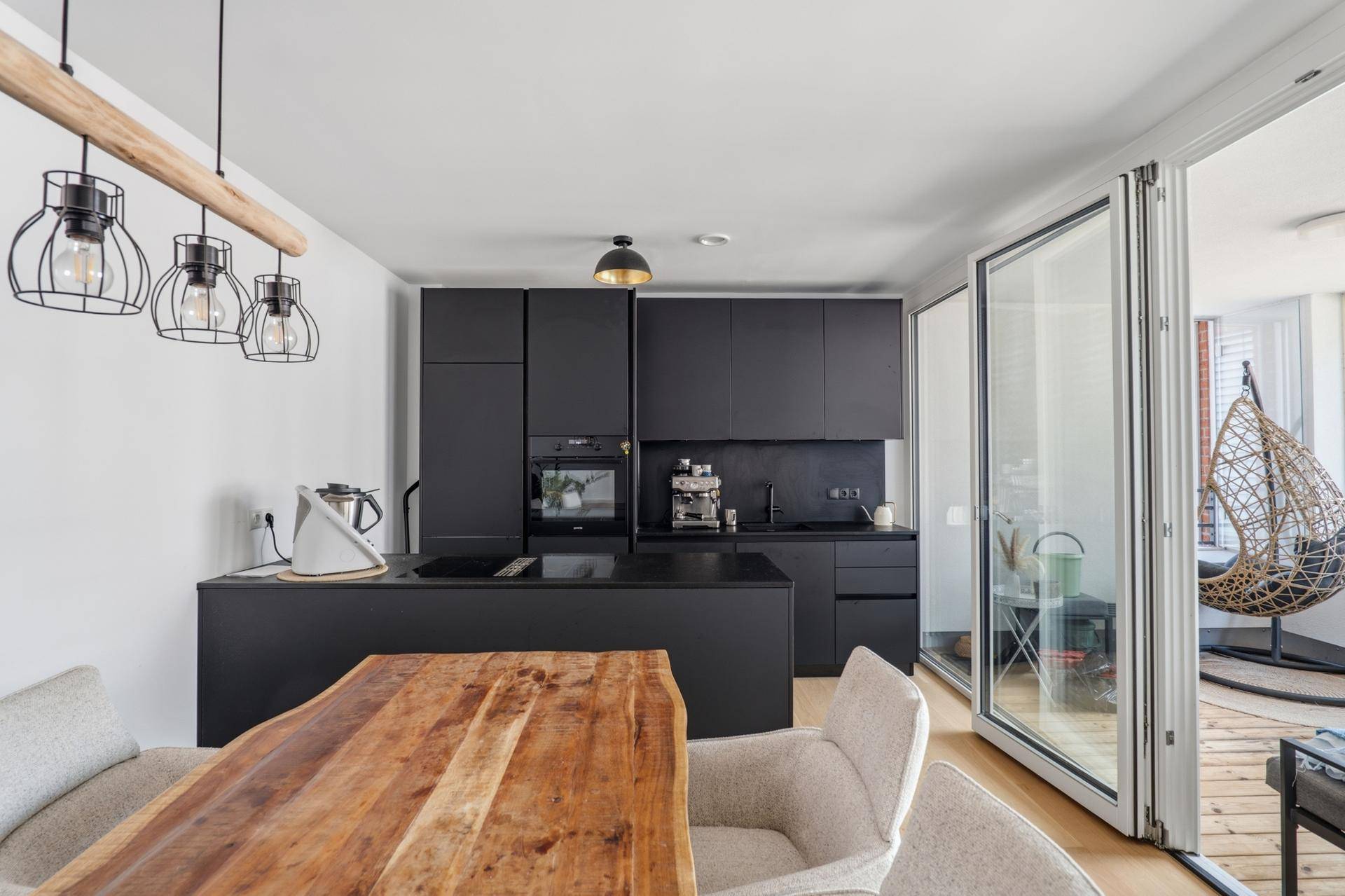 Moderne schwarze Einbauküche mit Kochinsel und Essbereich, offen zum verglasten Balkon.