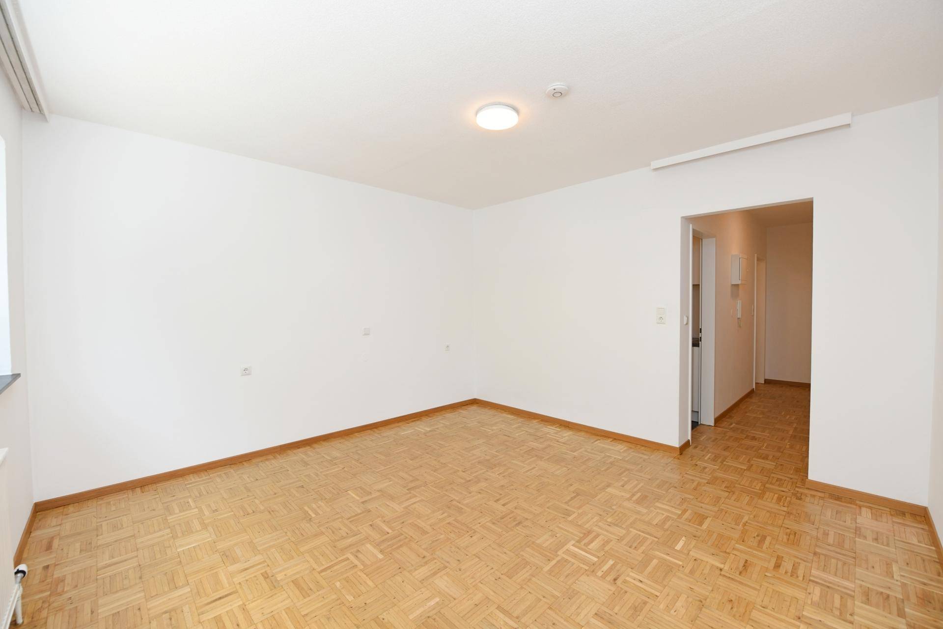 Geräumiger, leerer Raum mit Parkettboden und offenem Zugang zum Flurbereich.