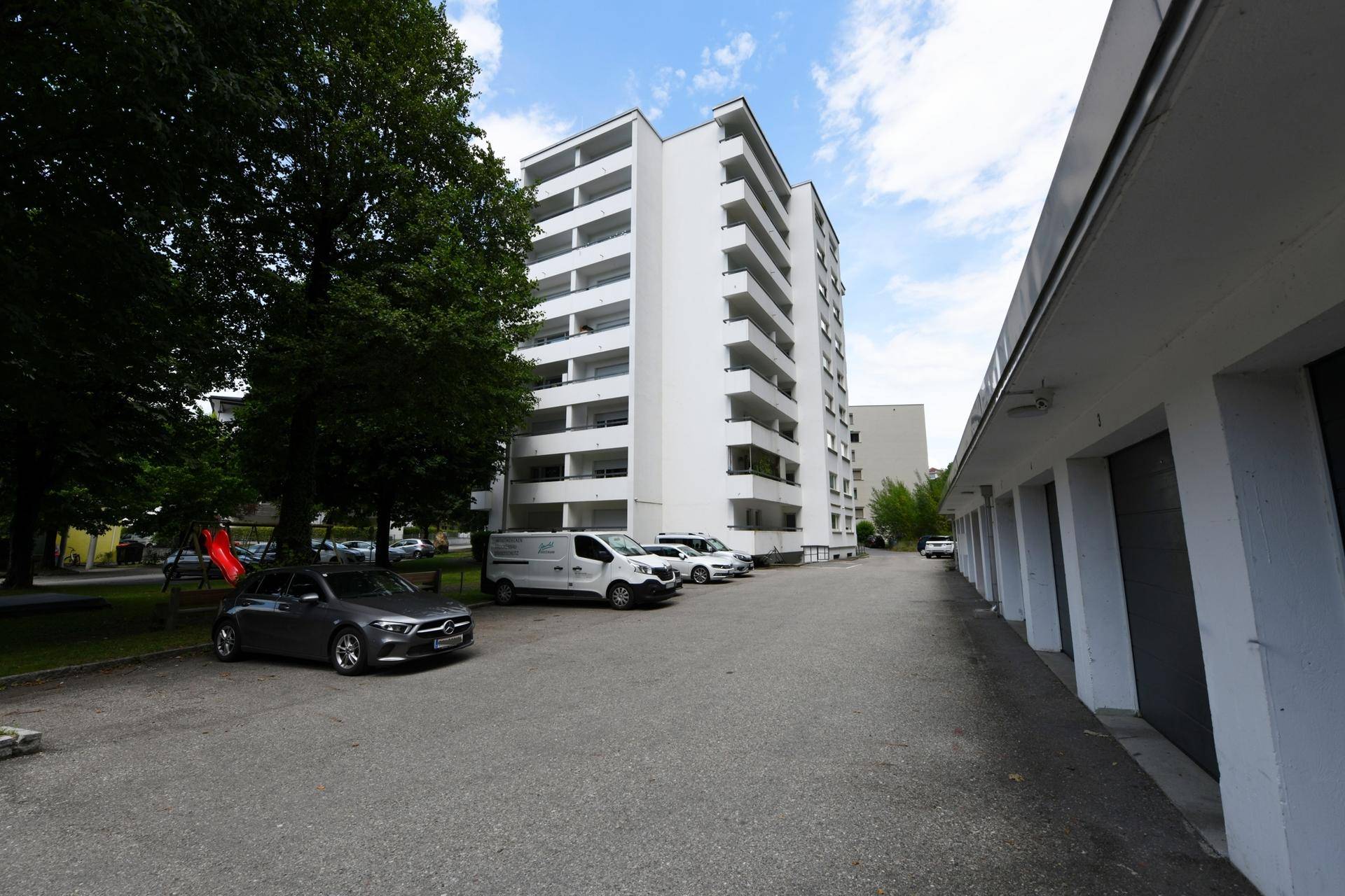 Weißes Wohngebäude mit Balkonen und angrenzenden Garagen sowie Parkmöglichkeiten.