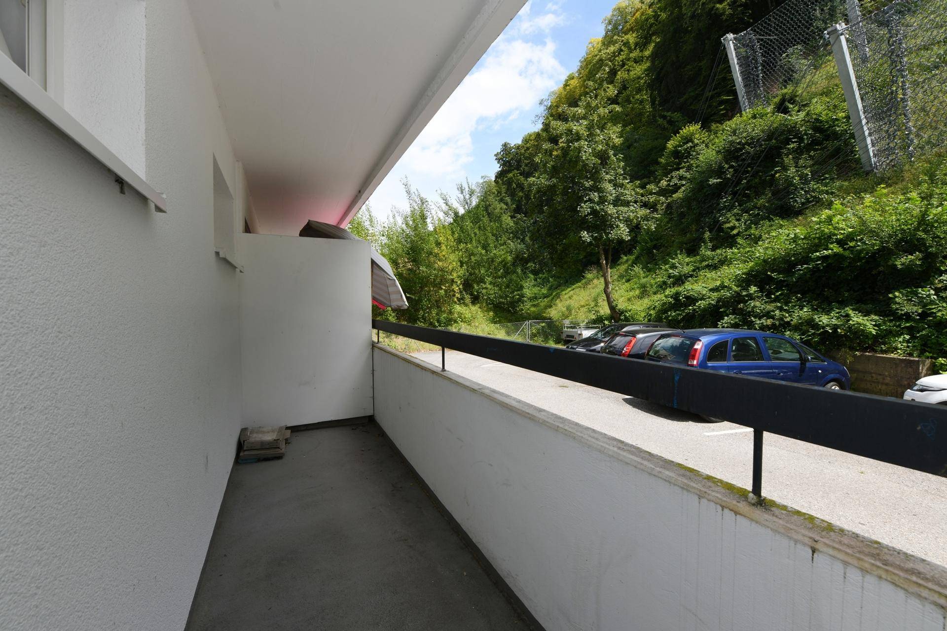 Langer Balkon mit Blick auf den Parkplatz und eine bewaldete Anhöhe.